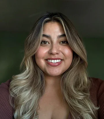 A smiling woman with long, wavy hair in front of a green wall.