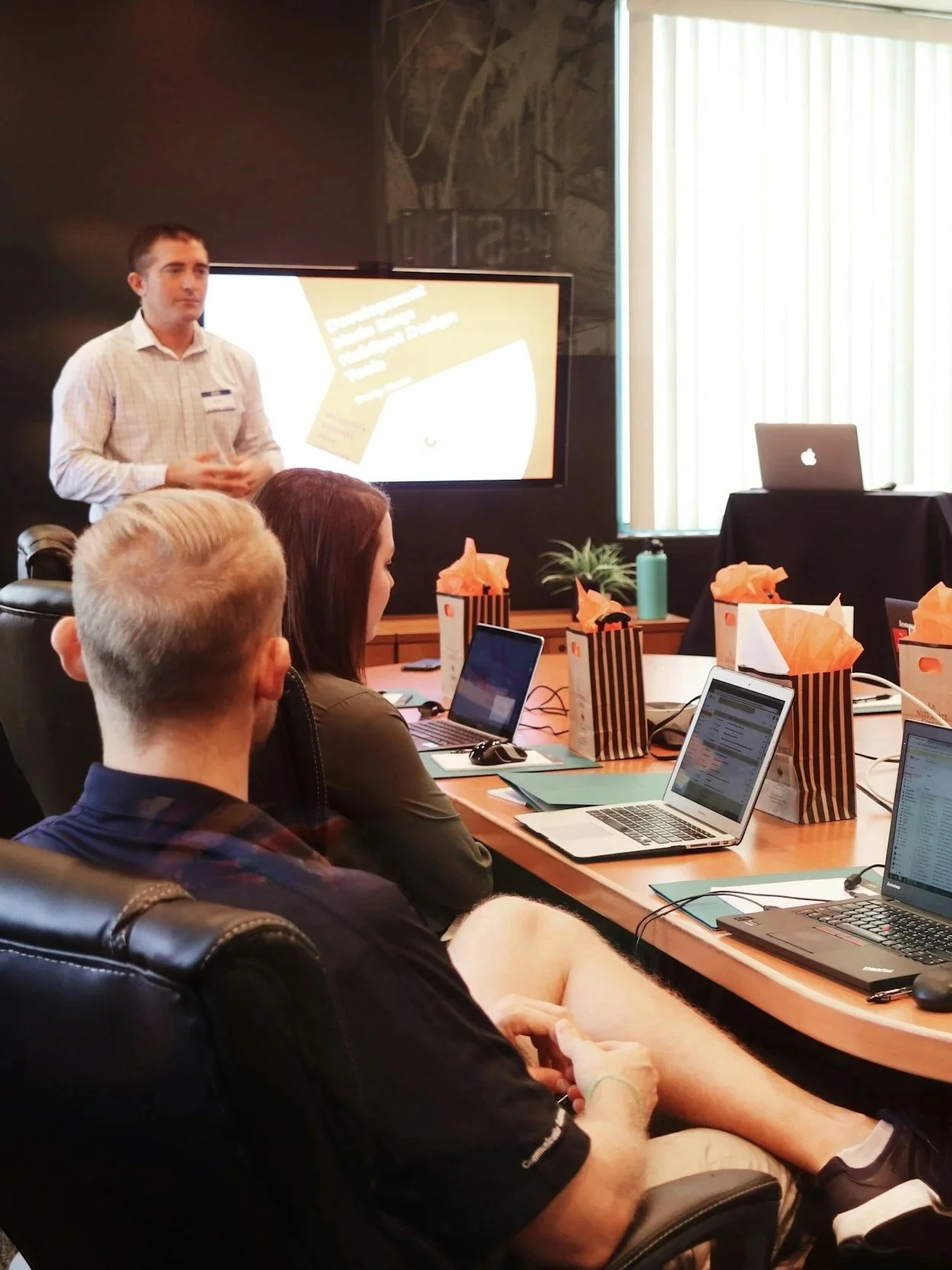 A man giving a presentation to a group of people in a conference room with laptops on the table.