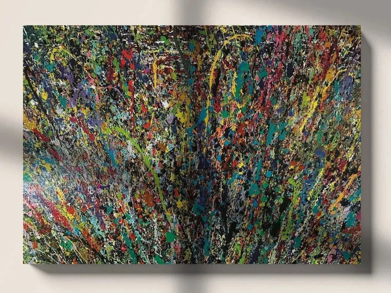 Abstract colorful splatter painting with vibrant reds, blues, yellows, greens, and blacks on a large canvas mounted on a wall.