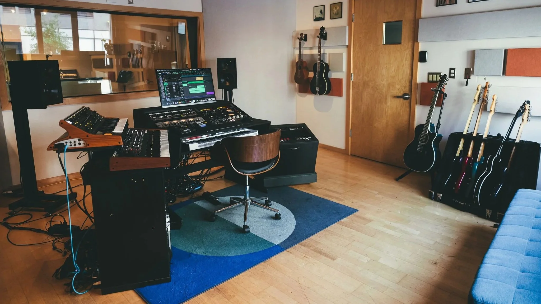 Music studio with a mixing console, computers, guitars, and a blue sofa.