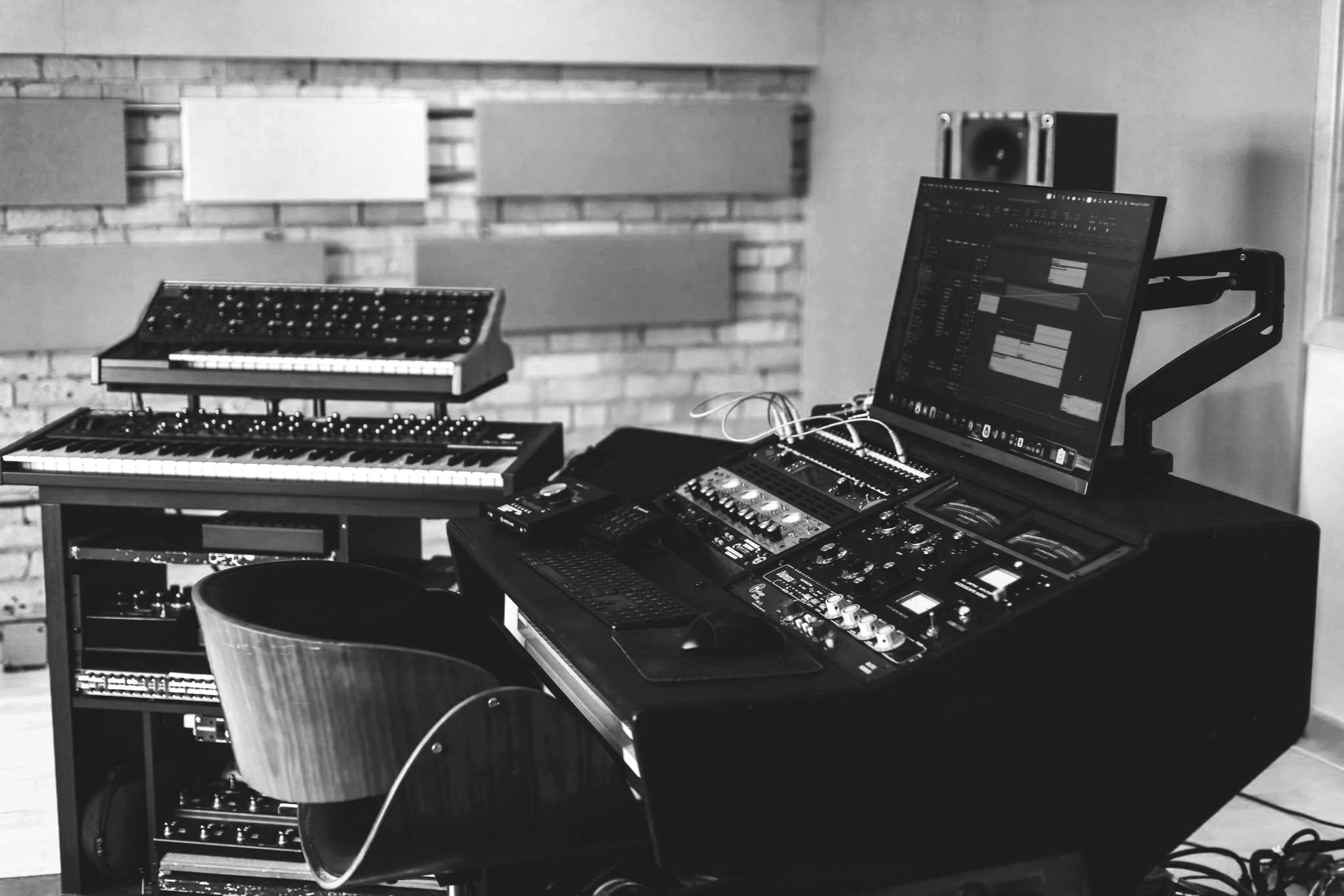 Music studio setup with a computer, synthesizers, and audio equipment in a room with brick walls.
