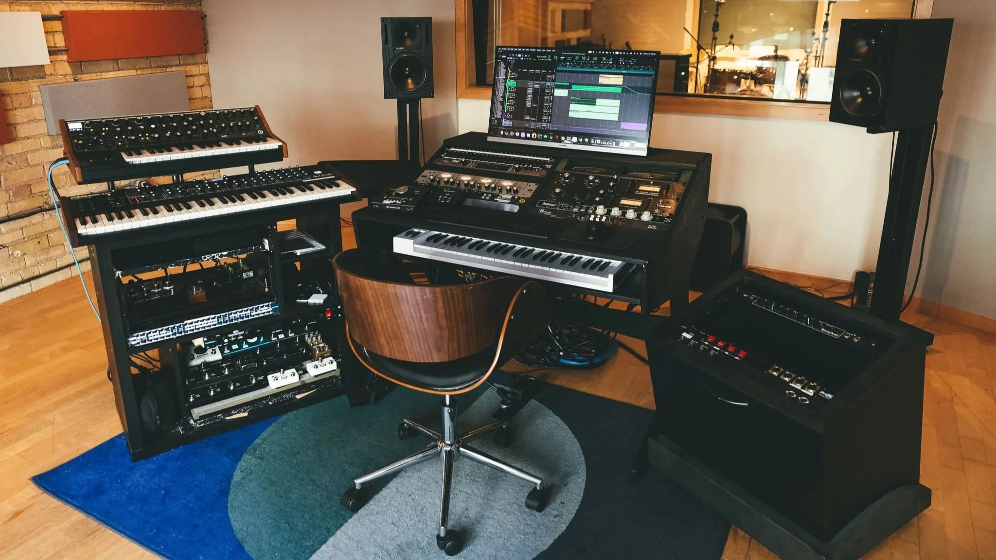 Music recording studio with multiple keyboards, a computer monitor displaying music production software, speakers, and audio equipment.