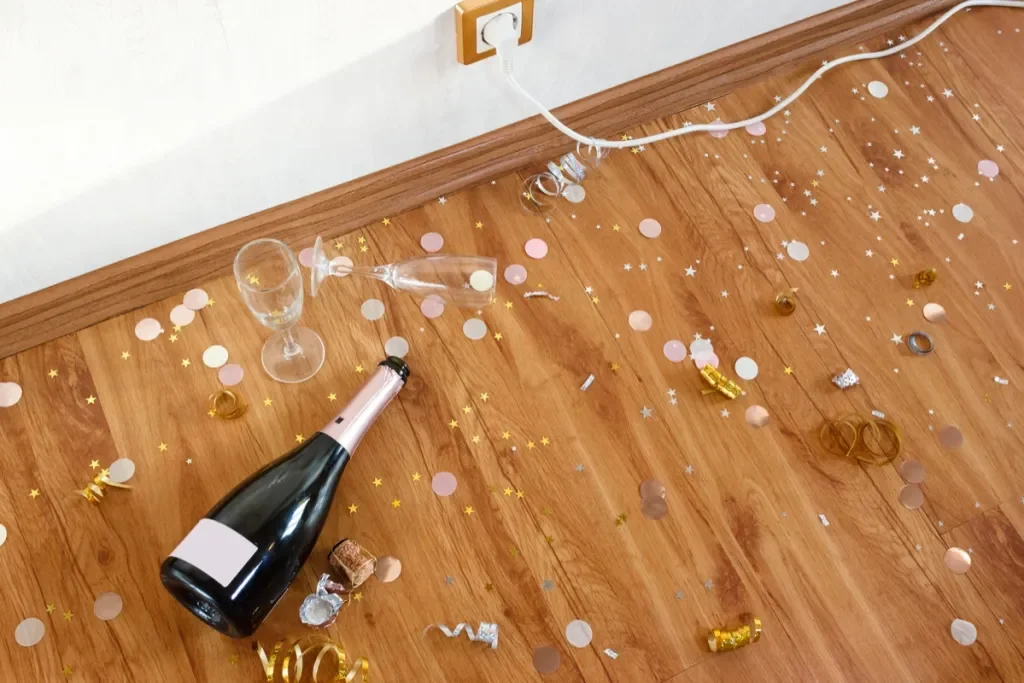 Décor de fête avec des confettis, une bouteille de champagne, des verres et des serpentins sur un sol en bois.