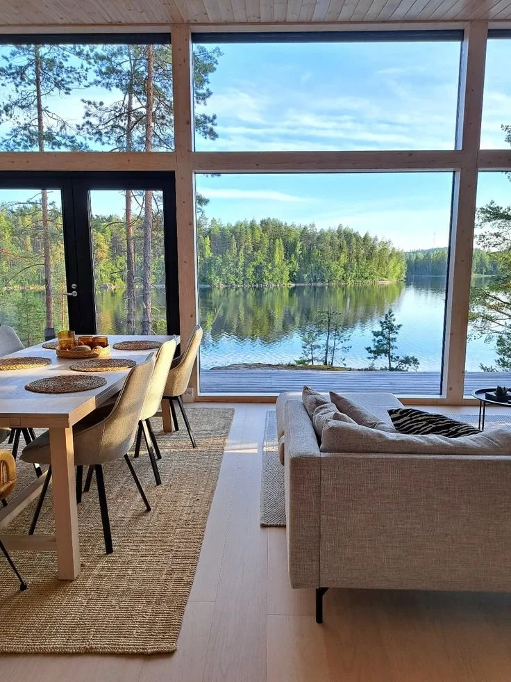 Salon avec vue sur un lac à travers de grandes fenêtres en bois.