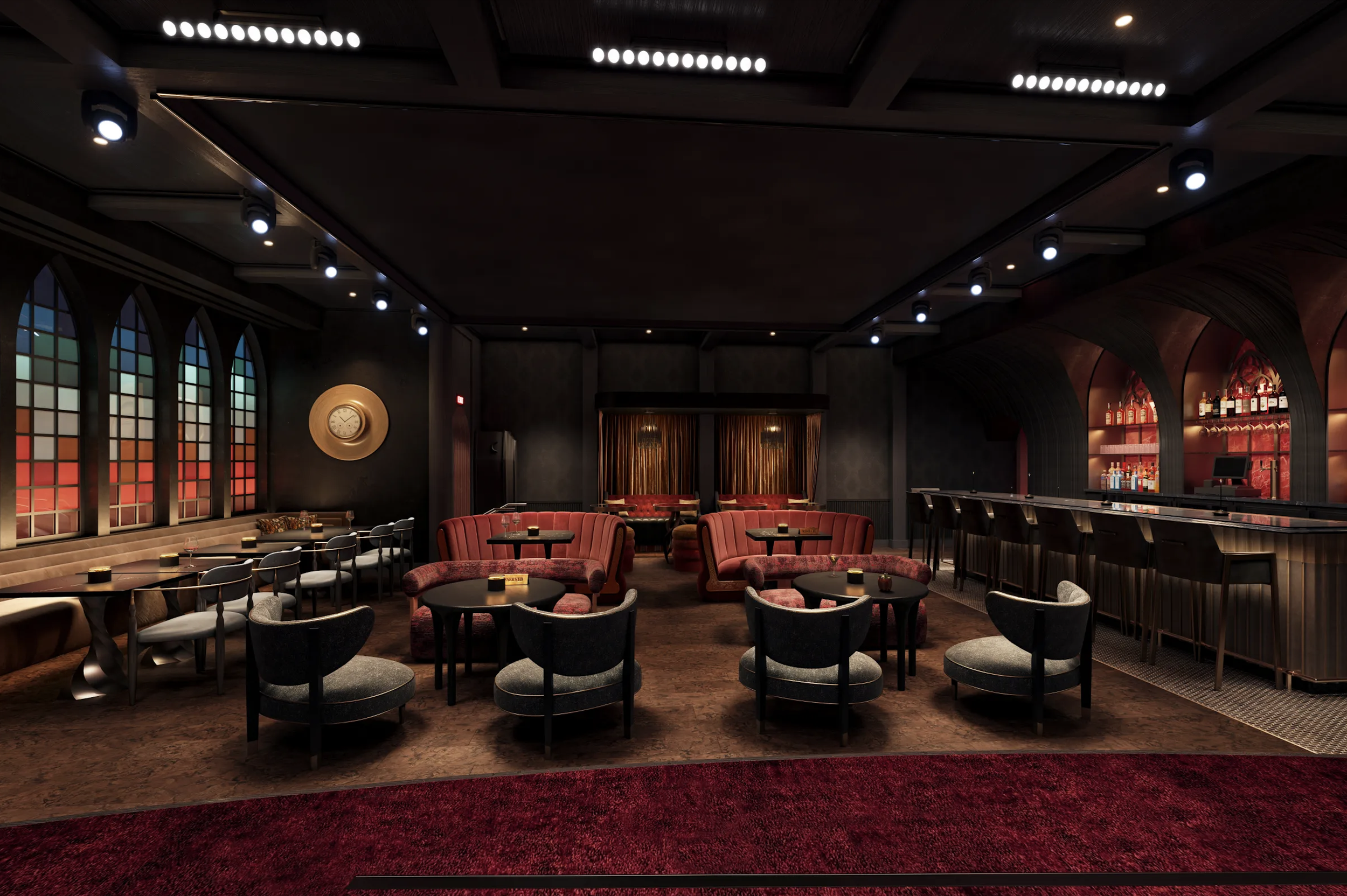 Interior of a dimly lit upscale bar or lounge with red velvet chairs, black tables, and a bar counter with various bottles of alcohol displayed. There are large arched windows with stained glass designs, a circular wall clock, and modern ceiling lights.