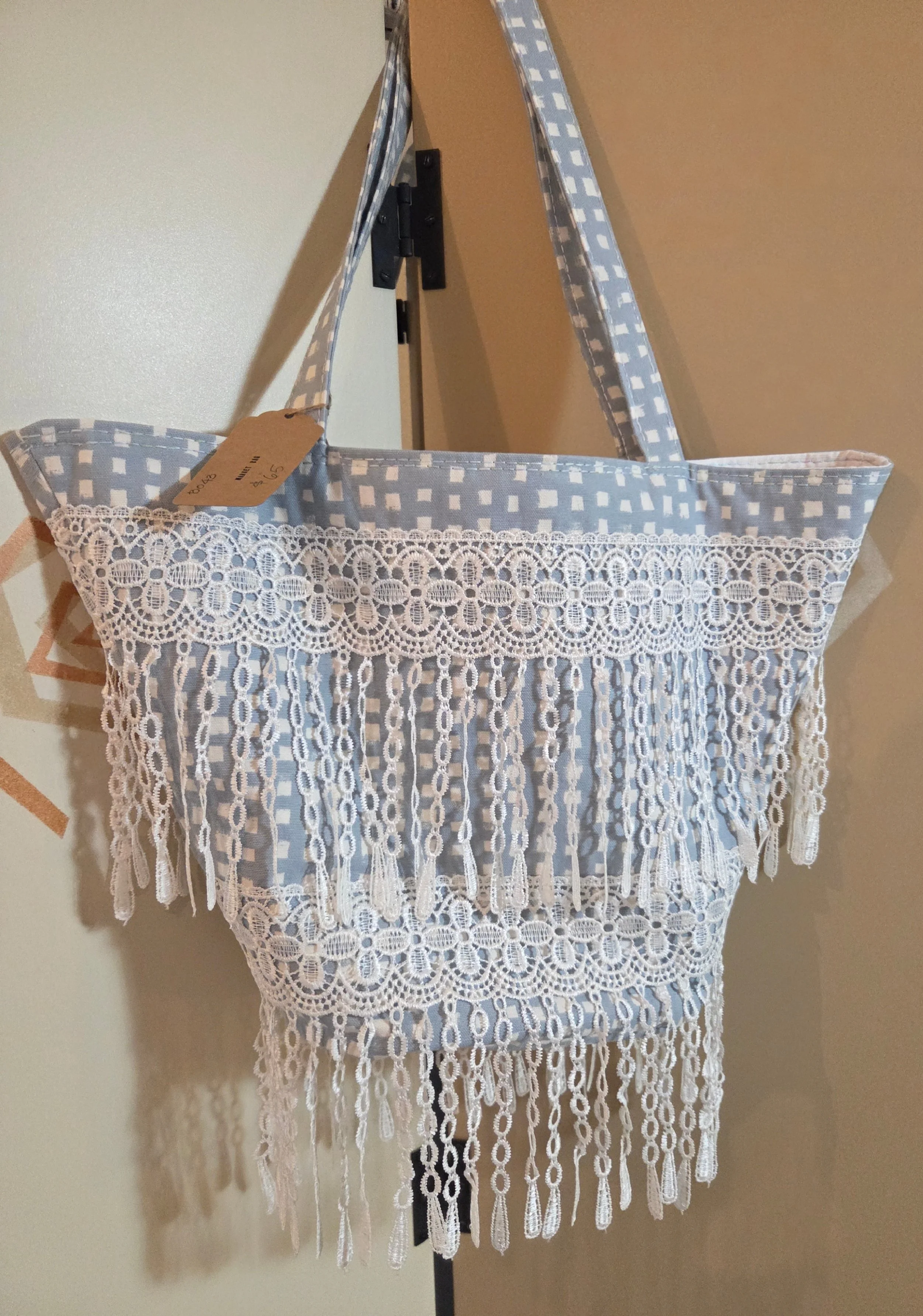 A light blue and white patterned tote featuring white lace and crochet trim with tassels at the bottom.