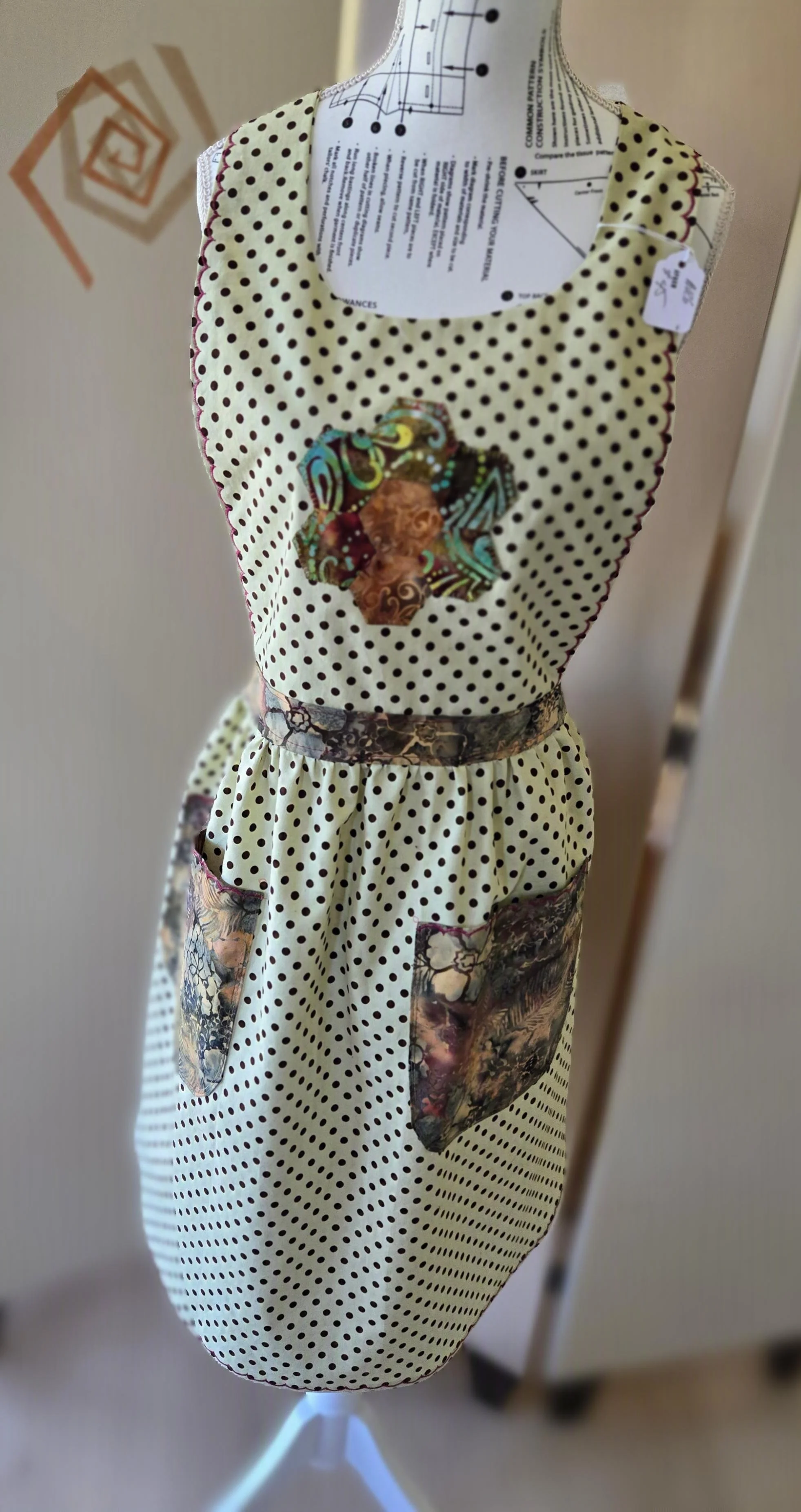 A mannequin displaying a  polka dot apron with floral print pockets and patchwork accents.