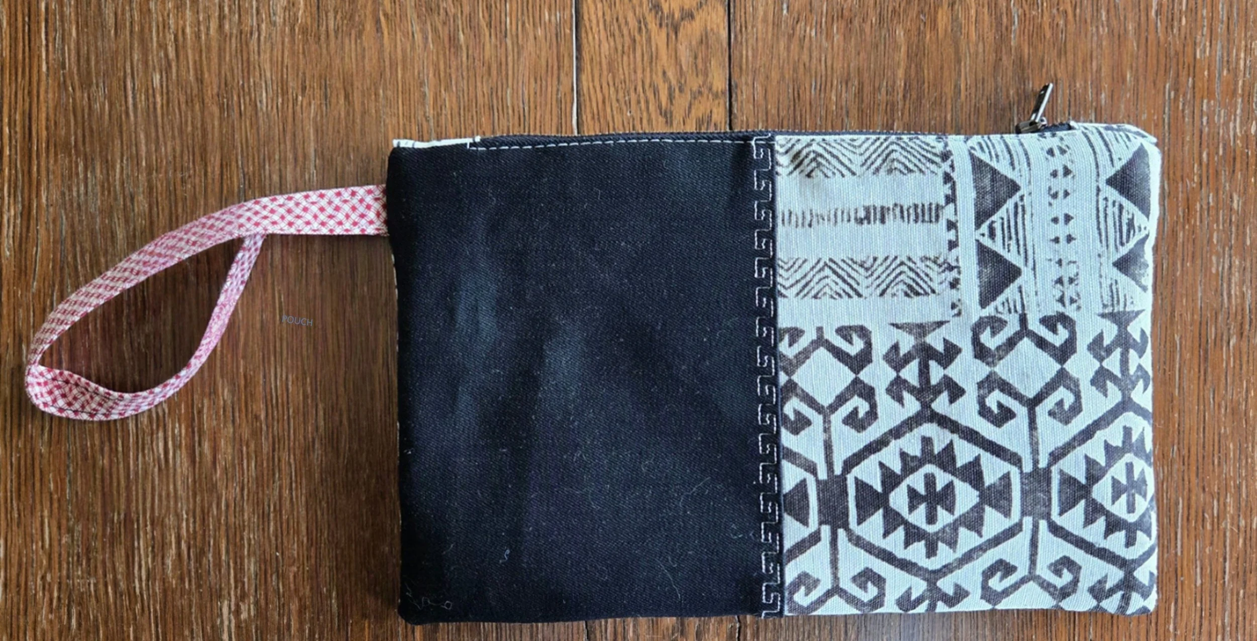 A fabric pouch made of black and light blue fabric, with a red and white checkered wrist loop, from dbfourdesign