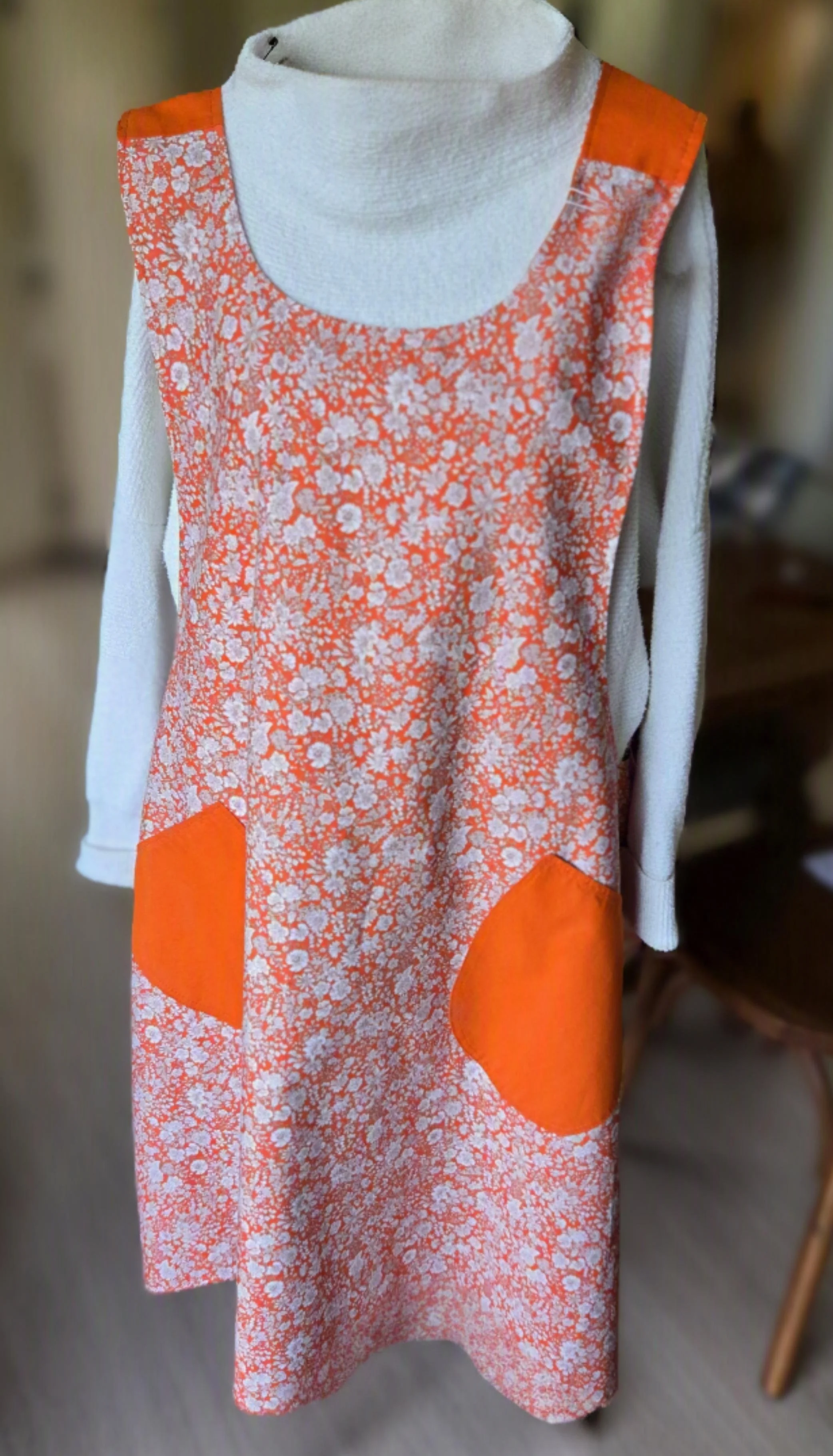A reversible apron for dbfourdesign with orange and white floral pattern and solid orange accents on the front pockets.