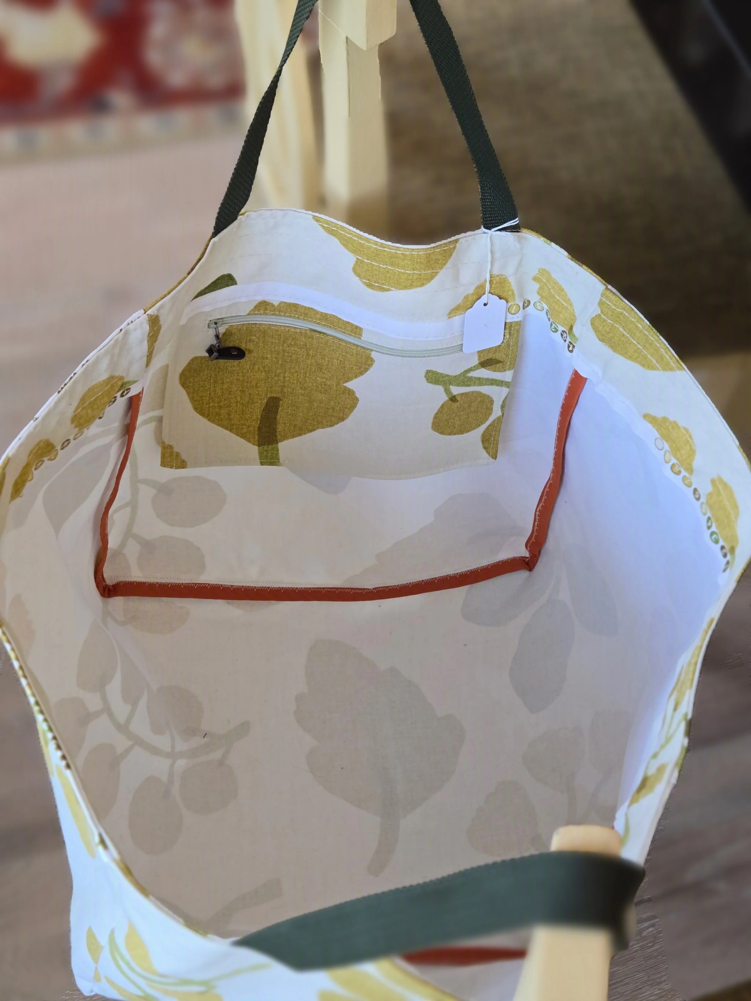 A close-up photo showing the interior of a fabric tote bag with a floral design in yellow, white, and green. The bag has a zippered pocket inside and black handles,from dbfourdesign