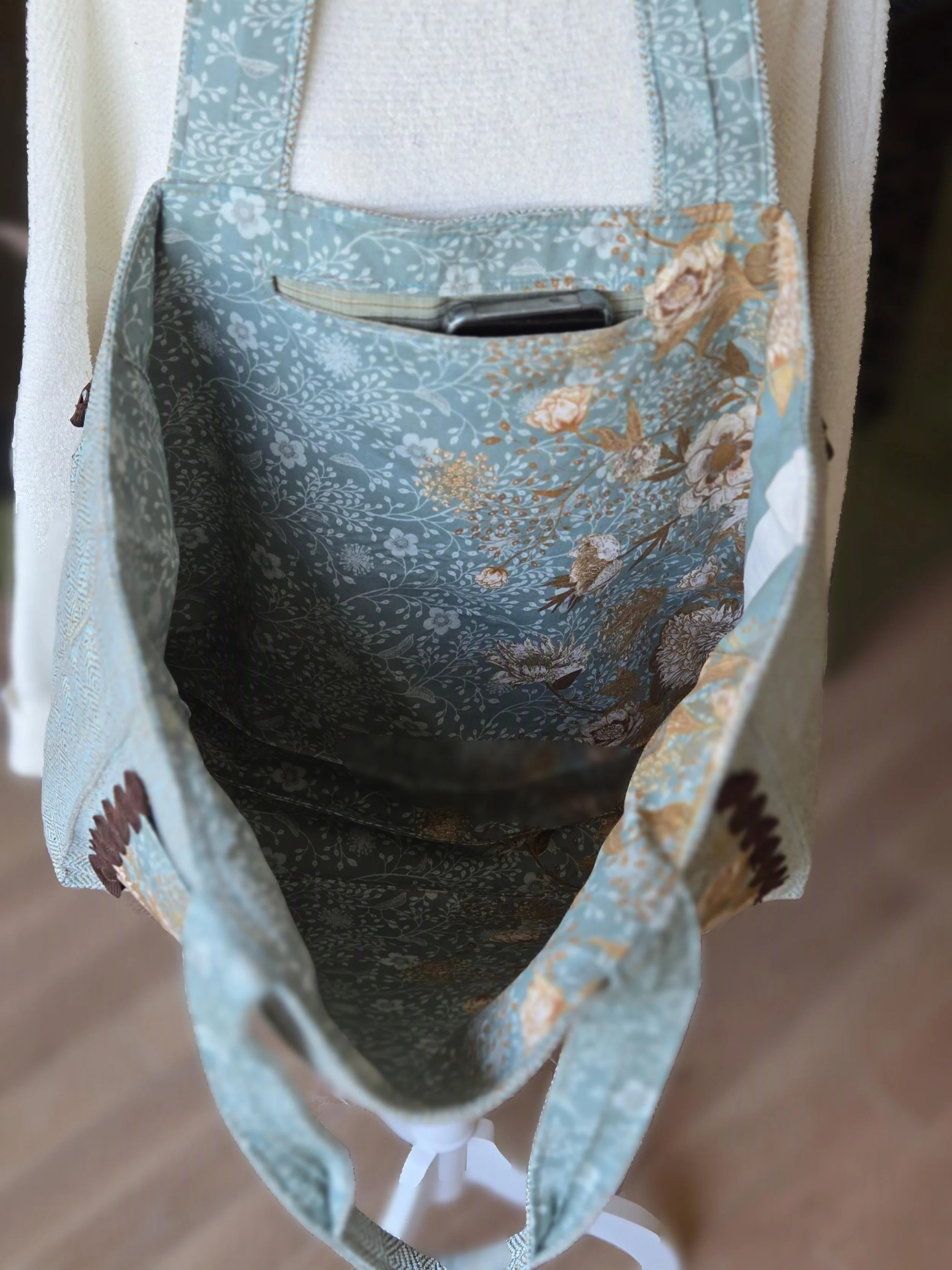 Inside of a fabric bag with a floral and bird pattern, holding a smartphone. SIze matters and this will hold a day of shopping. from the studio of dbfourdesign