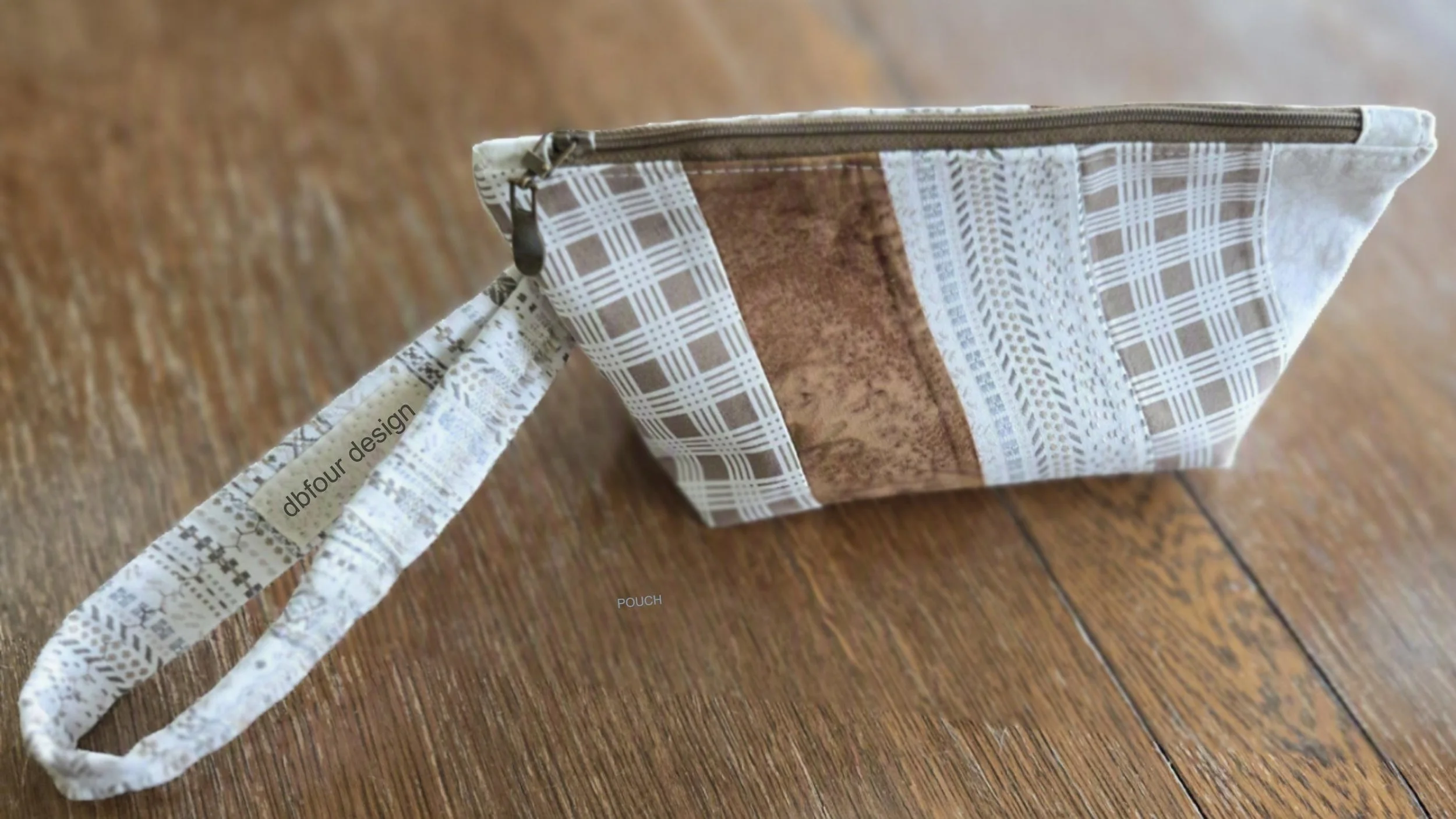 A fabric pouch featuring a geometric pattern with shades of brown, white, and beige, with a zipper at the top and a wrist strap attached for just the essentials, brought to you by dbfourdesign