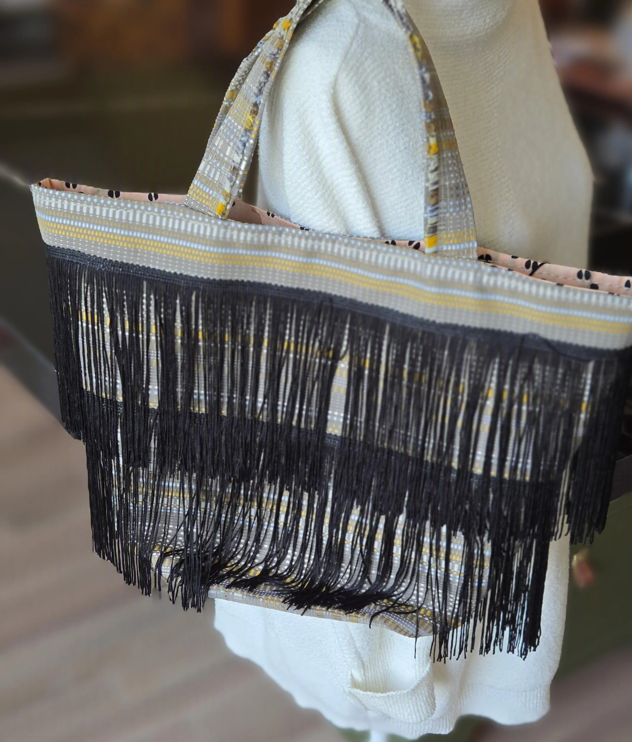 Fabric tote bag with black fringe, yellow, white, and gray pattern. dbfourdesign