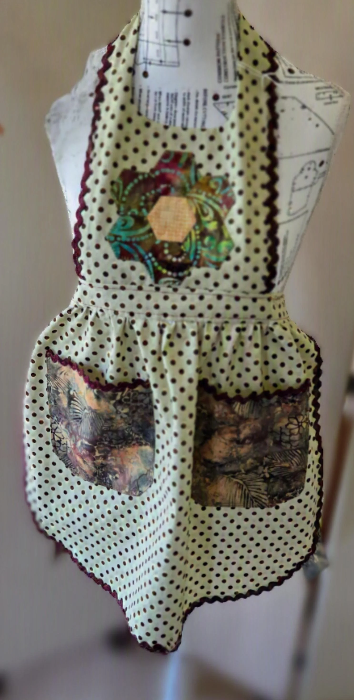 A green apron with black polka dots, featuring colorful fabric patterns in the pockets and a floral design in the center, also available in kids size just so they can look like mom. dbfourdesign