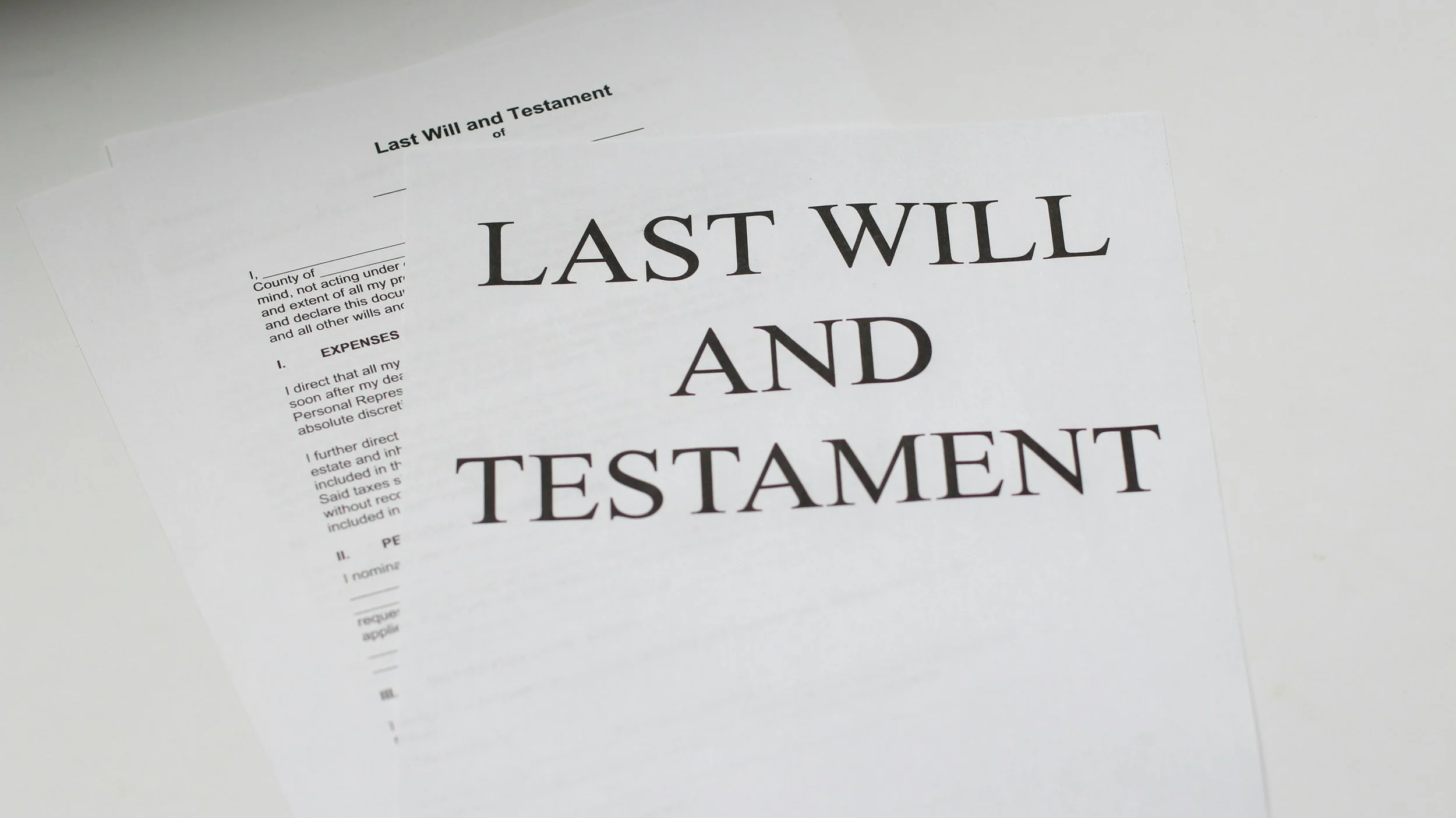 A close-up photo of a Last Will and Testament document with bold text, partially overlapping another document on a white surface.