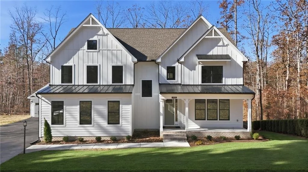 A modern two-story house with white siding, black window frames, and a black metal roof, surrounded by a well-maintained lawn and trees in the background.