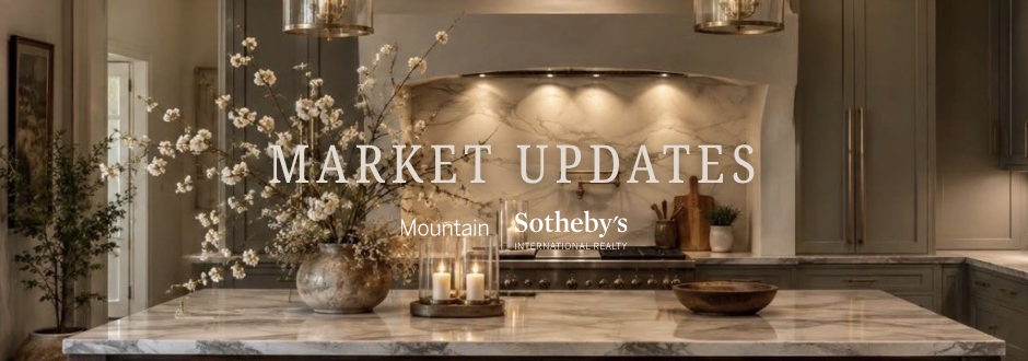 Interior of a kitchen featuring a marble countertop, decorative flowers, candles, and modern cabinetry, with overlay text 'Market Updates' and 'Mountain Sotheby's International Realty'.