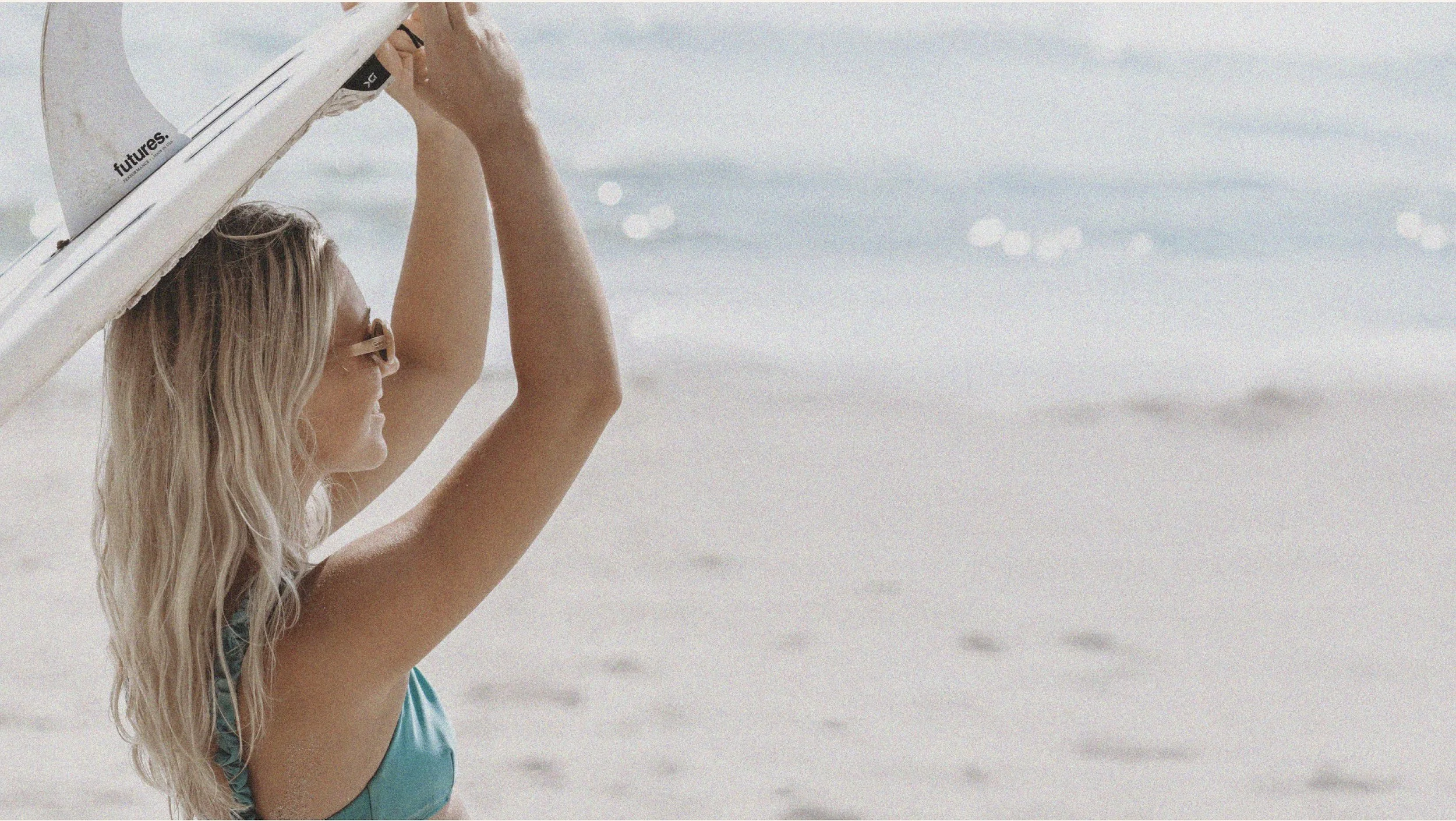 Brand image of blonde woman with a surfboard looking at the waves