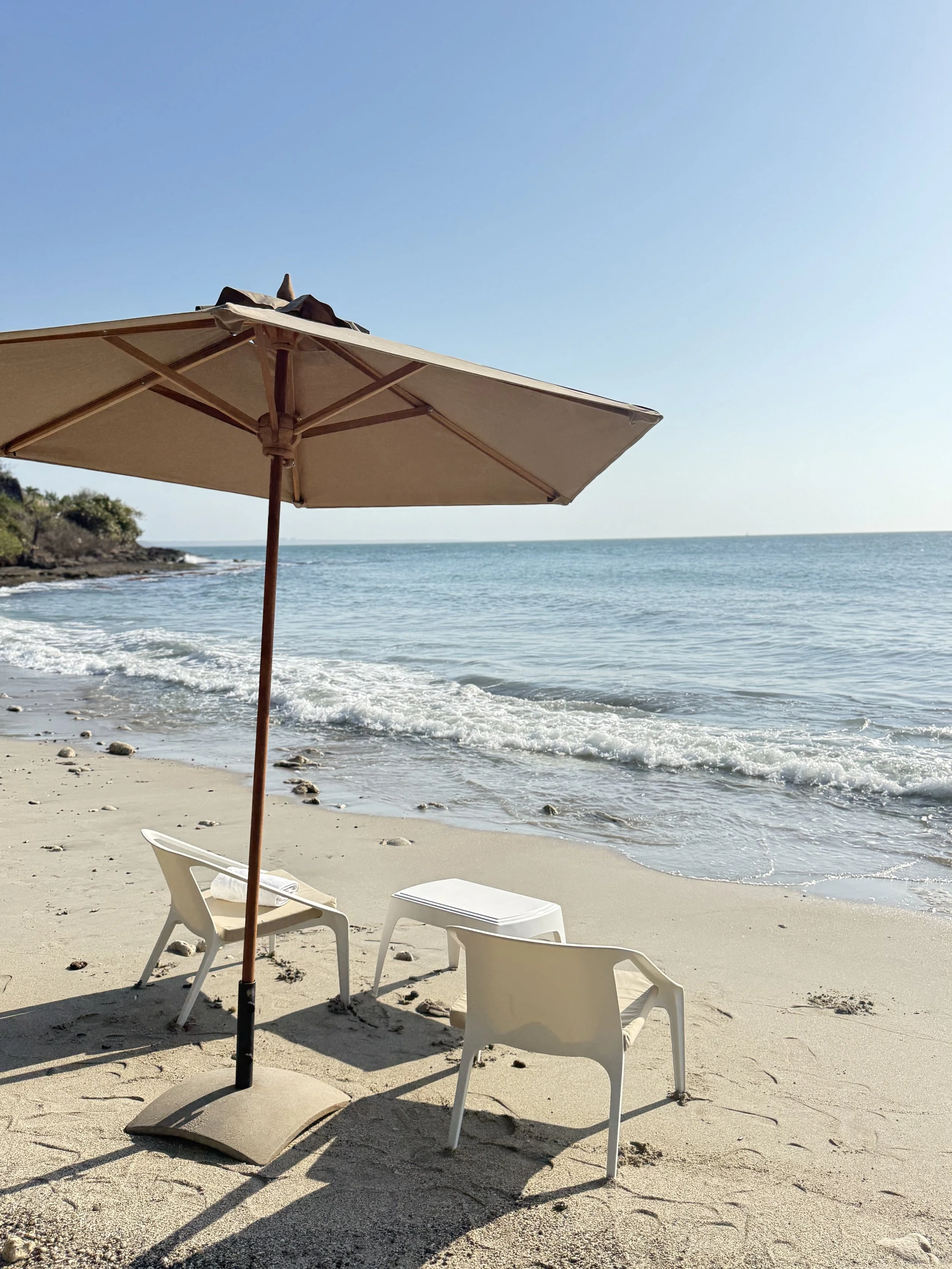Sombrilla de playa, sillas y mesas en la orilla del mar con arena blanca.