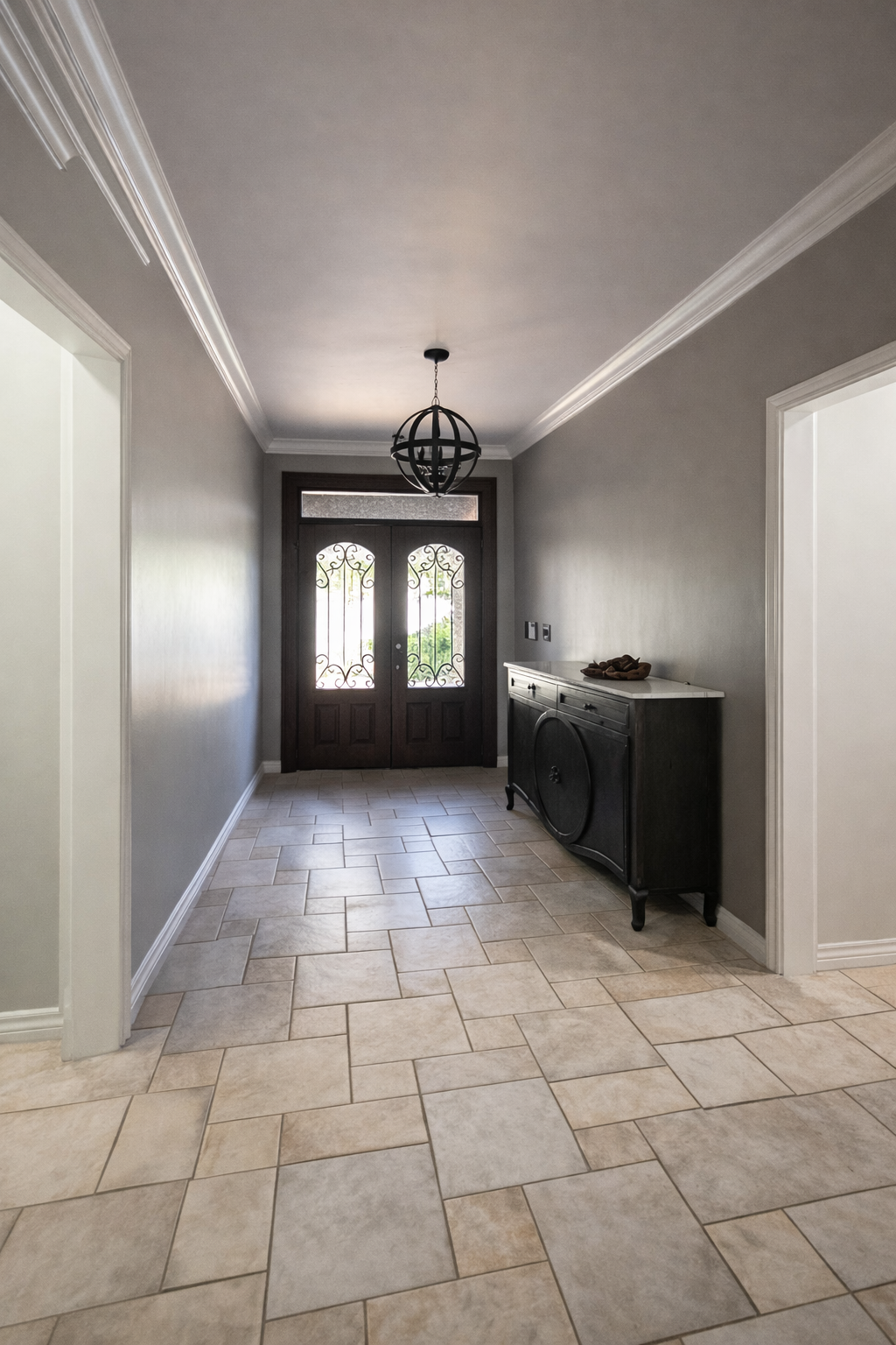 Entryway with beige tiled floor, gray walls, a dark wood front door with decorative glass and wrought iron details, a black chandelier hanging from the ceiling, and a black sideboard on the right side.