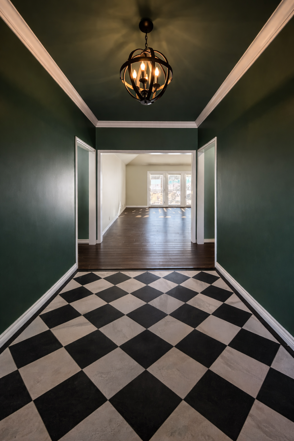 Entryway with black and white checkered tile floor, green walls, and a hanging chandelier. Opens into a bright room with hardwood floors and large windows.