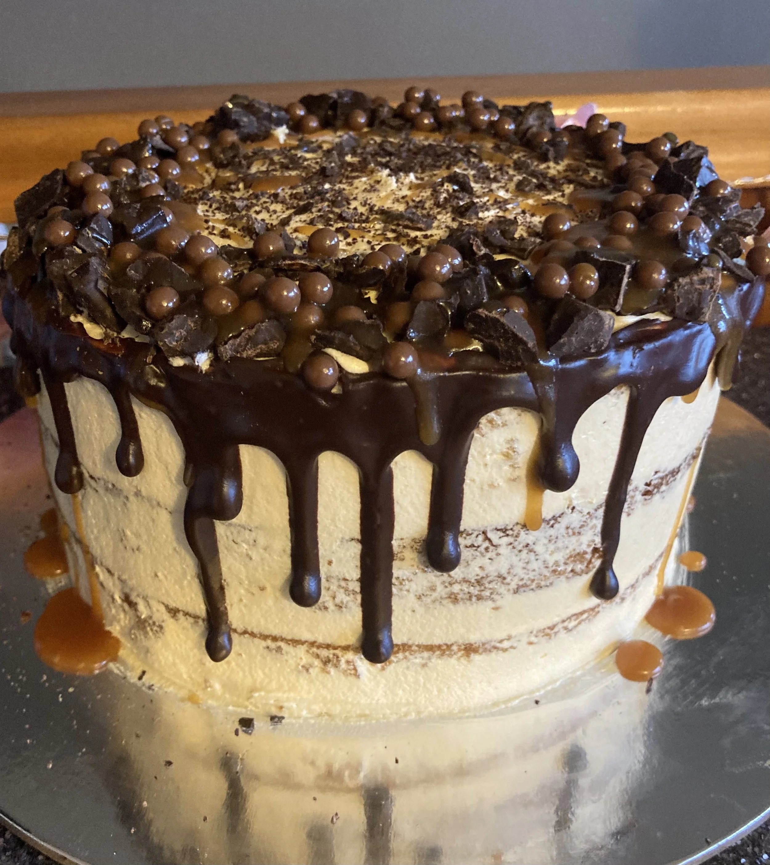 A cake decorated with chocolate chips, chocolate chunks, and caramel or butterscotch dots, with chocolate drizzle on the sides.