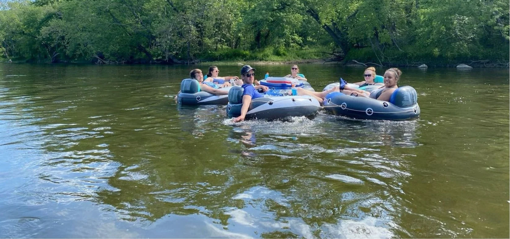 Six people relaxing on inflatable tubes in a river with trees in the background.