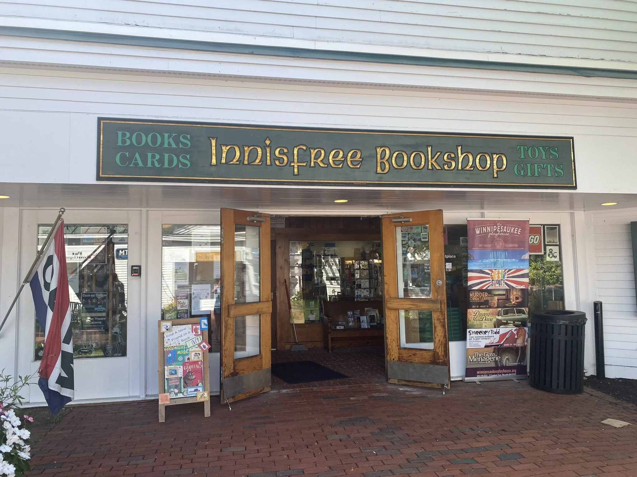 The exterior of a 'Innisfree Bookshop' in Meredith with a sign for their books, cards, toys, and gifts.