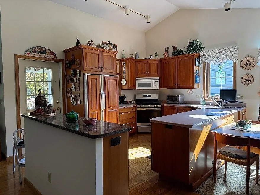 Kitchen with wooden cabinets, a central island, a microwave, toaster, and computer near the window, decorated with plates and plants.