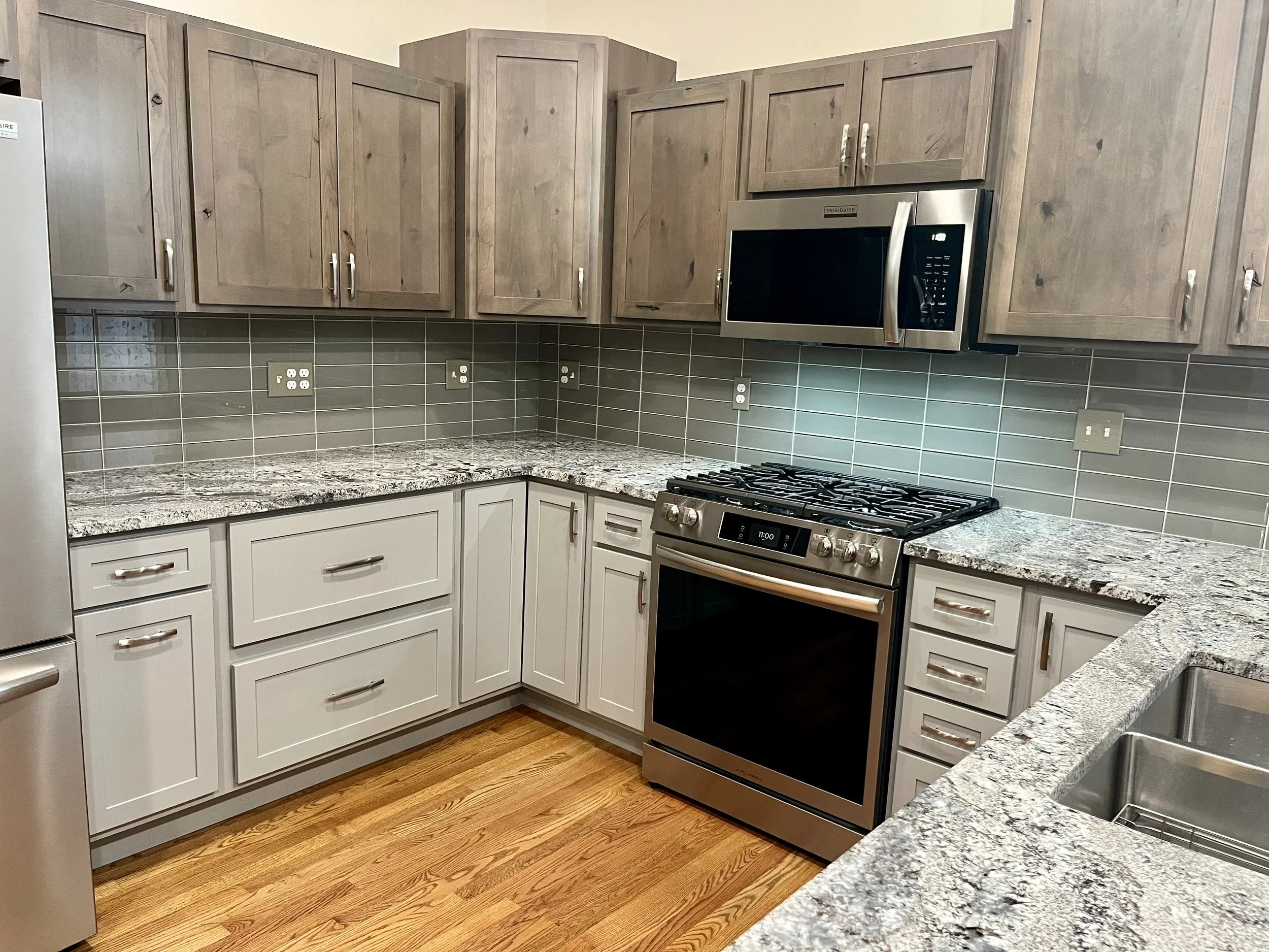 A modern kitchen with wooden cabinets, a granite countertop, a stainless steel microwave oven, a gas stove, and electrical outlets on a tiled backsplash.