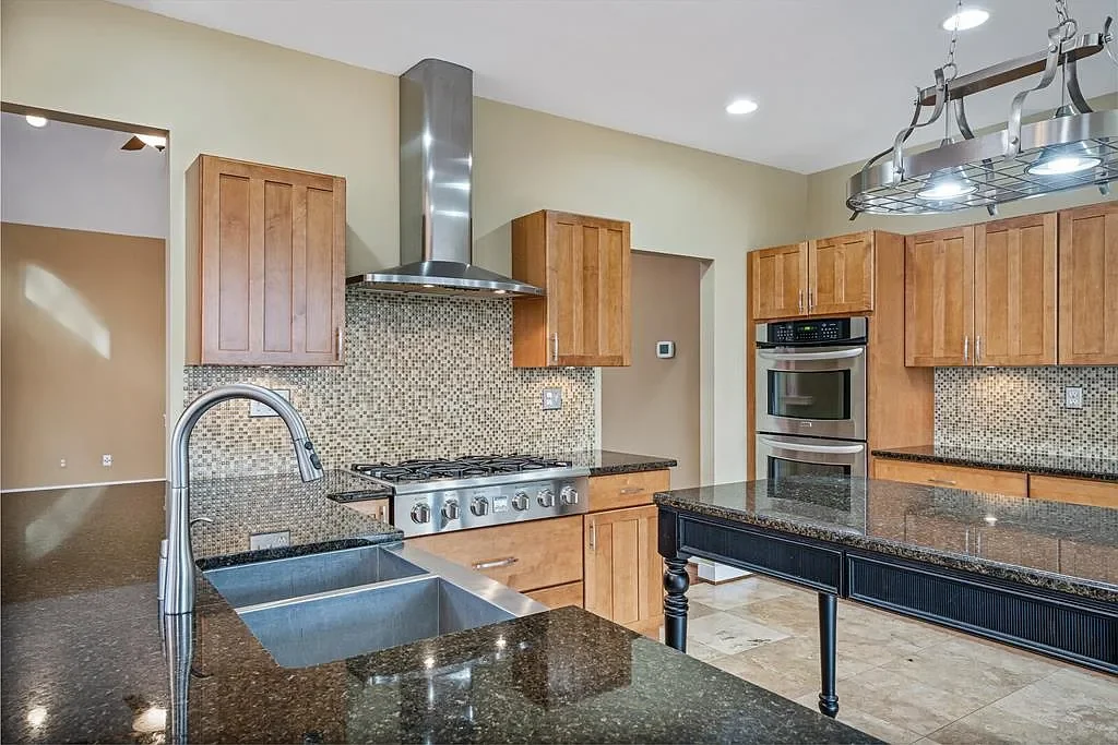 Modern kitchen with wooden cabinets, stainless steel double oven, gas stove, granite countertops, mosaic tile backsplash, and a large kitchen island.