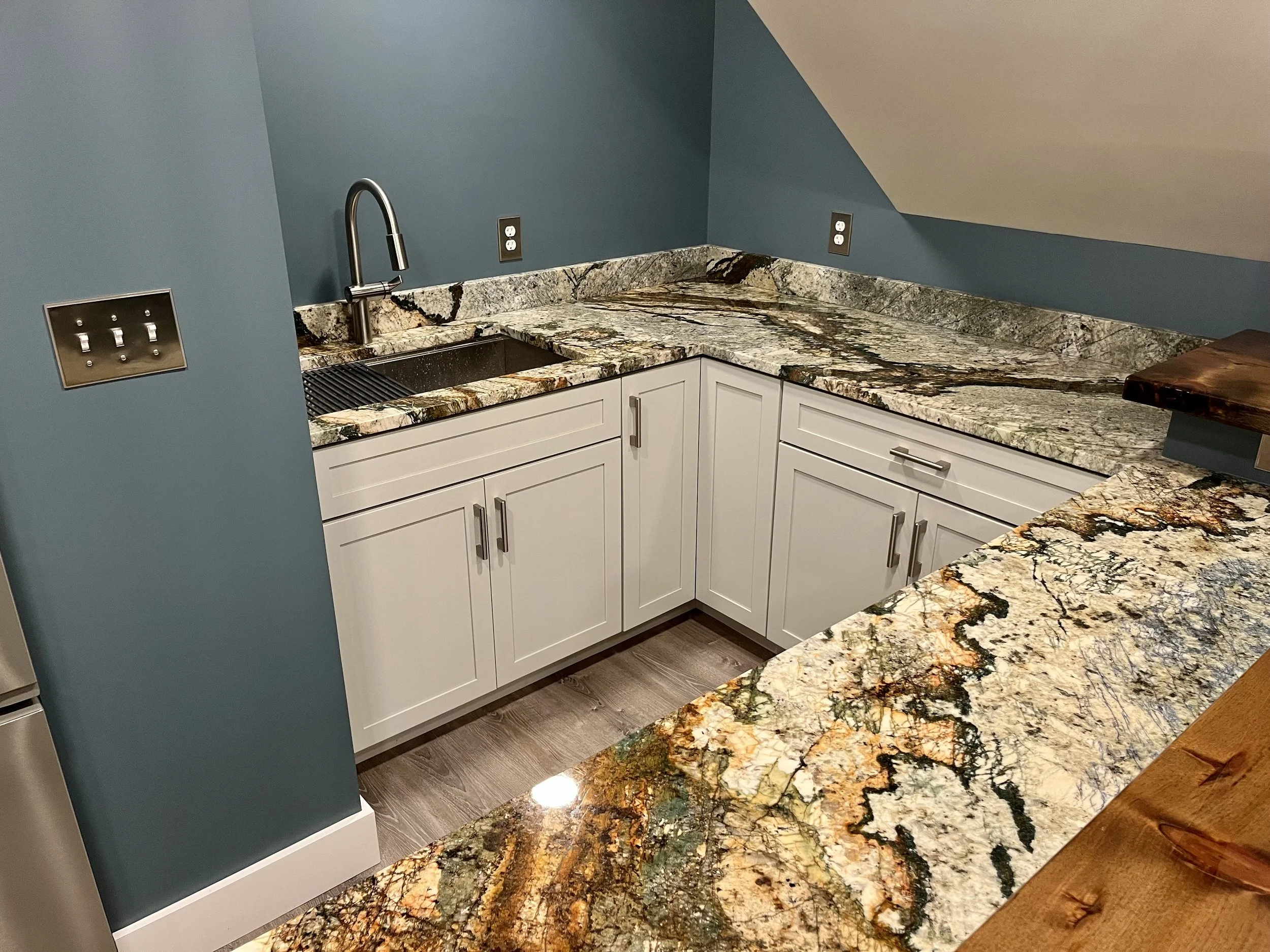 Close-up of a kitchen countertop with a colorful, patterned granite surface, backsplash, and white cabinets underneath.