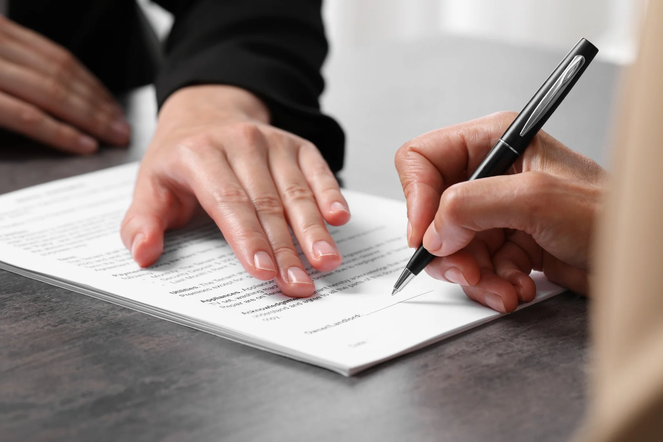 Close-up of a person signing a document with a black pen, resting their hand on over the paper.