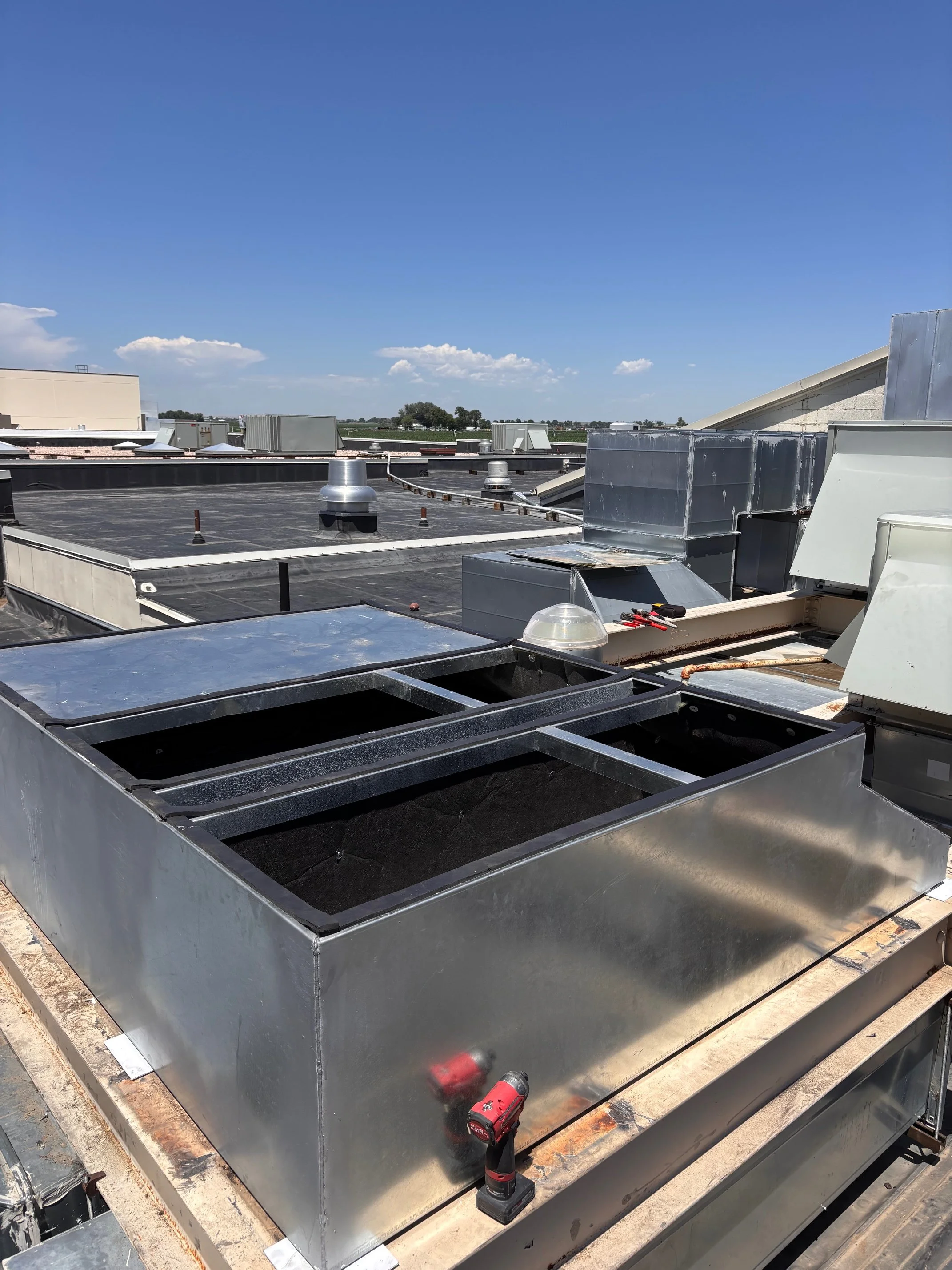 Rooftop with HVAC curb adaptor and ductwork, a drill, and tools on a sunny day.
