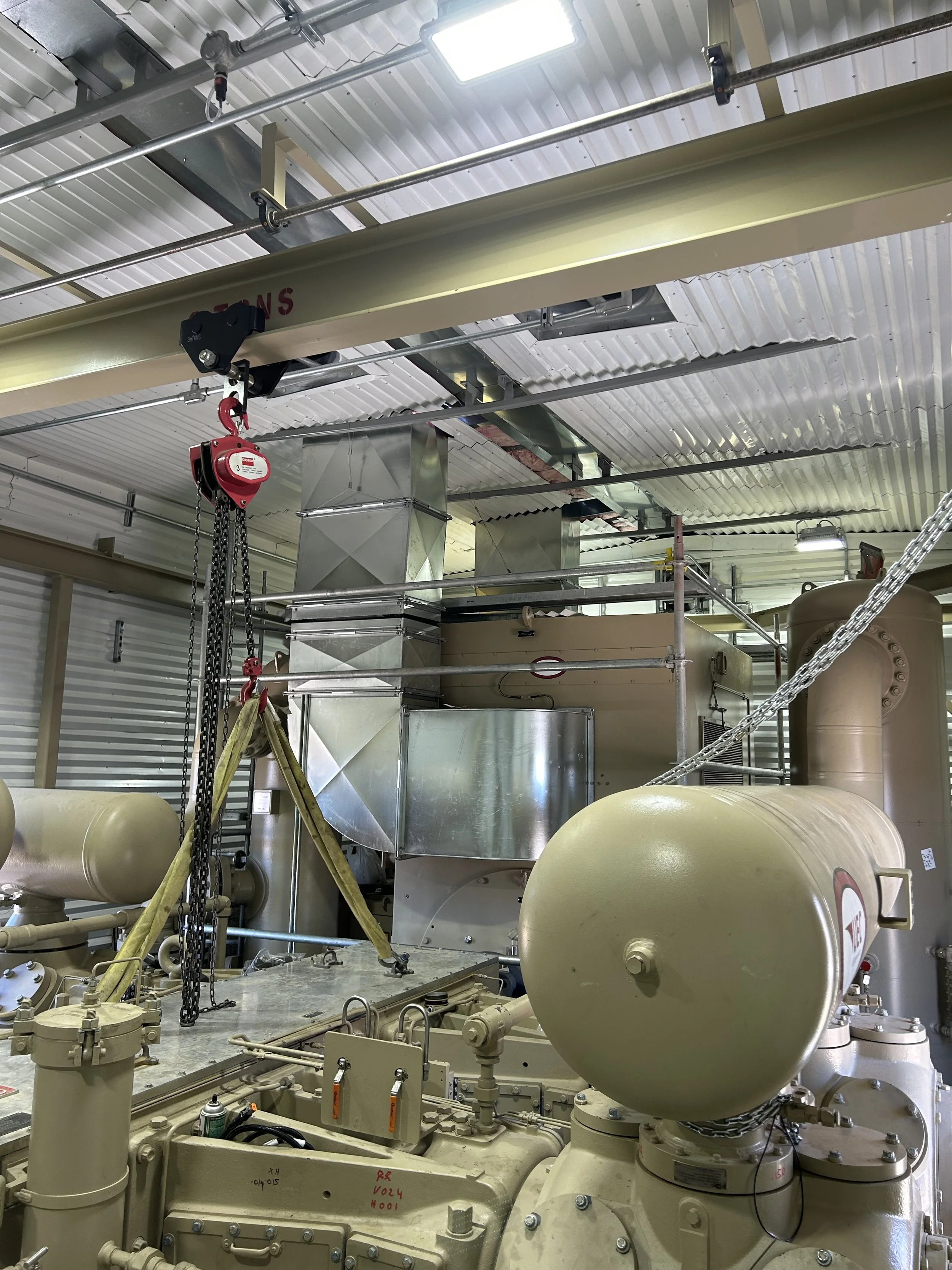 Industrial air compressor with ductwork, pipes, large tanks, and a lifting device in an instrument air building.