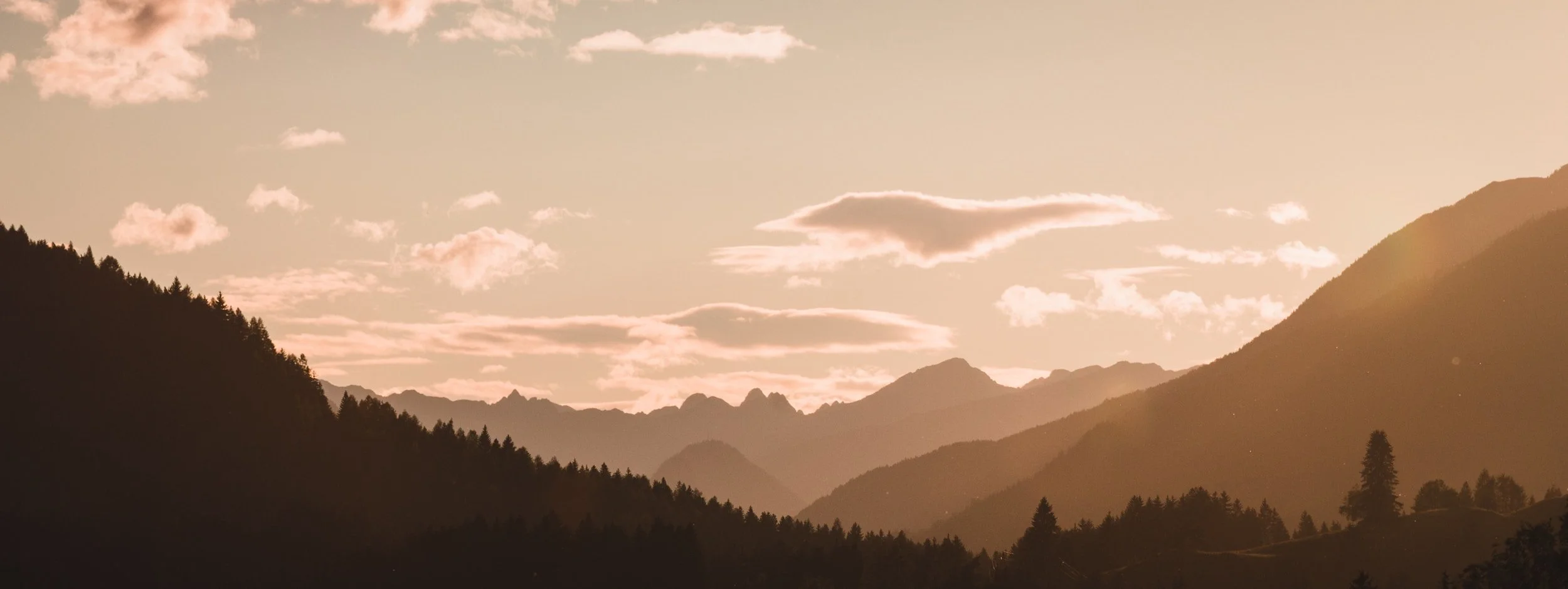 Sunset over a mountain range with scattered clouds and layers of dark and light hills.
