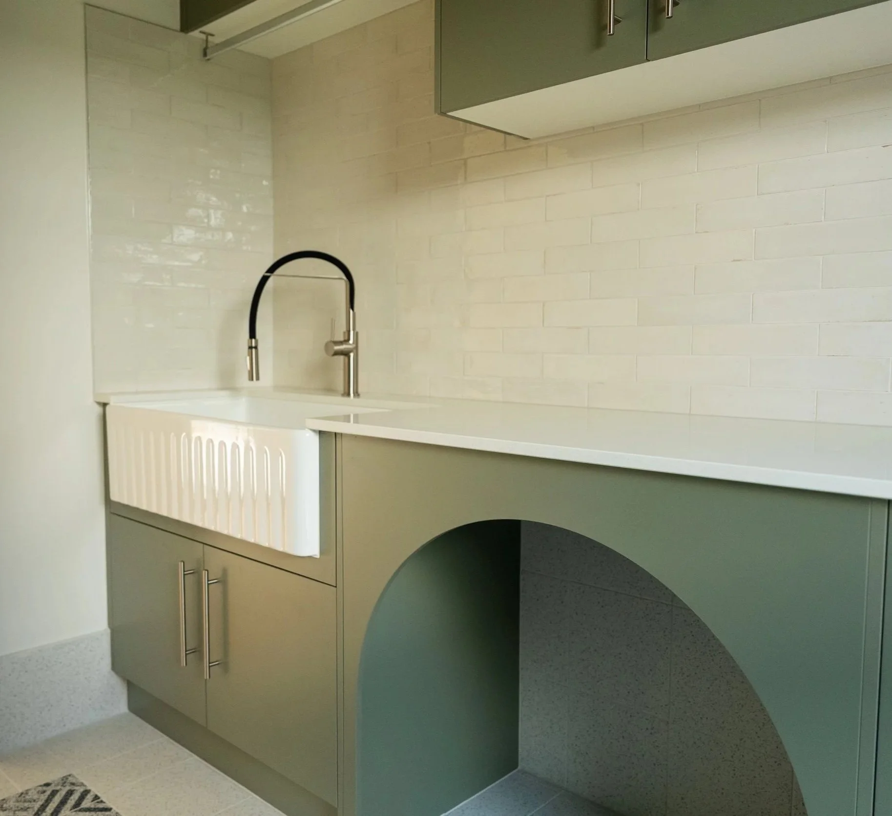 Kitchen with beige cabinetry, a white countertop, a black curved faucet, and a white tile backsplash.
