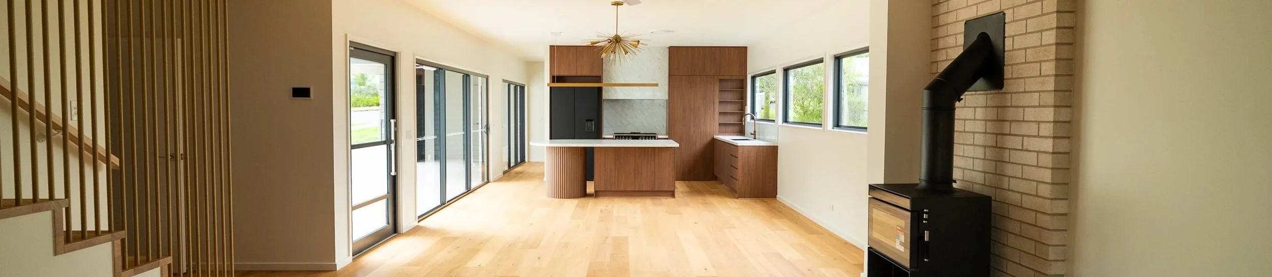 Open-concept living area and kitchen with wooden floors, modern cabinetry, sliding glass doors, and a brick accent wall with a black wood stove.