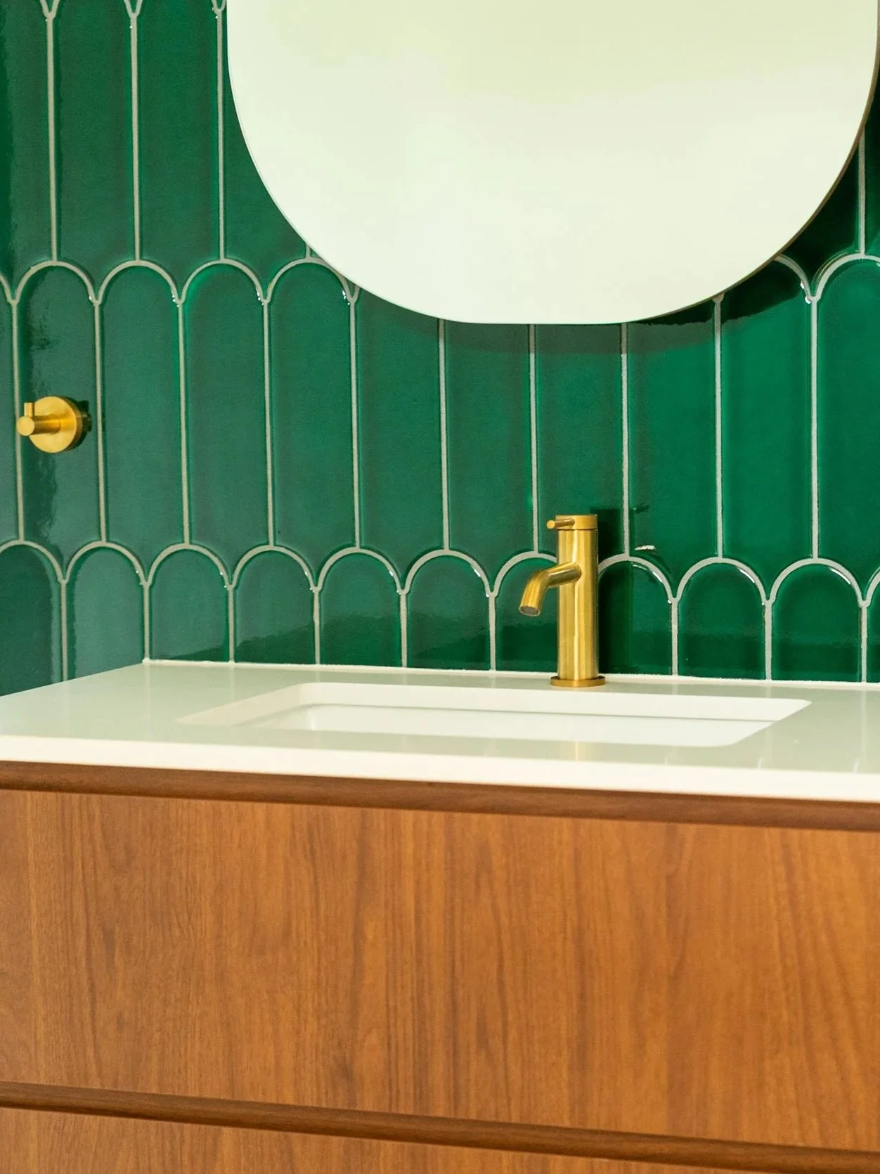 Close-up of a bathroom sink with a gold faucet and a green tiled wall in the background.