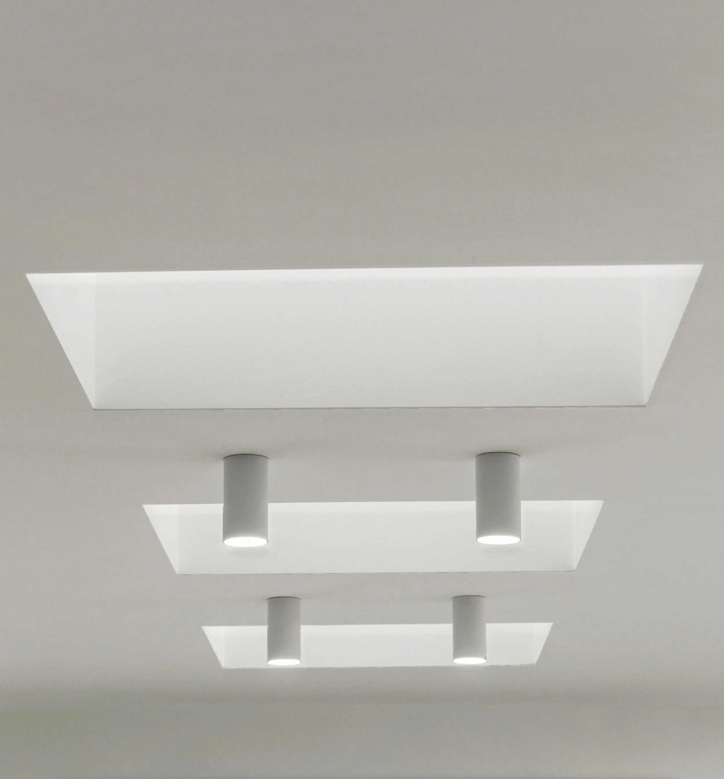 Ceiling with four white cylindrical recessed lights and rectangular skylights in a modern building.
