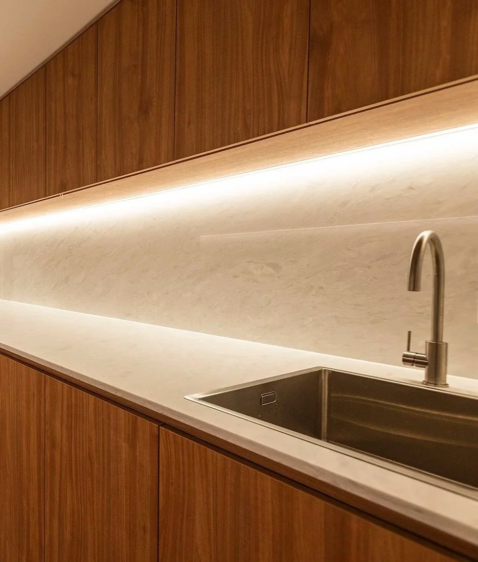Modern kitchen with a wooden cabinet, a white countertop, a beige backsplash, and a stainless steel faucet over a sink.