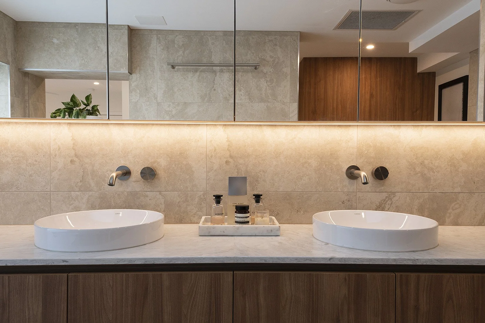 Modern bathroom with dual vessel sinks, beige tiled walls, and a large mirror.