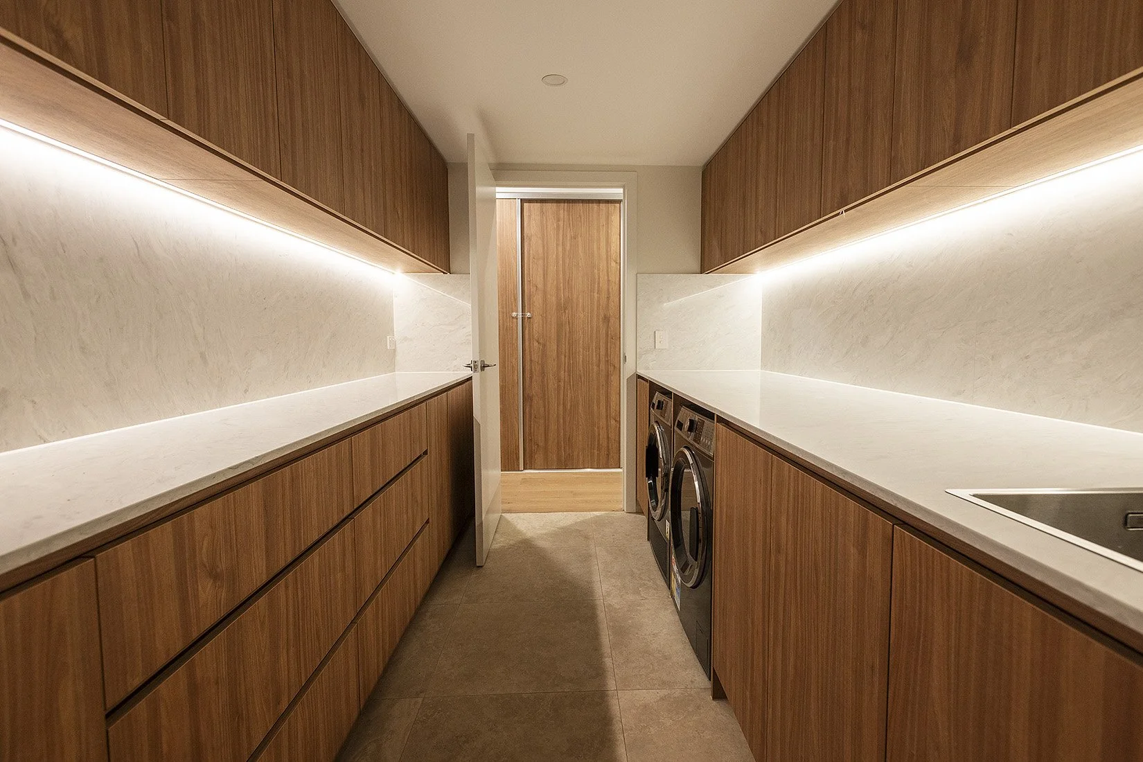A modern laundry room with wooden cabinets and drawers on both sides, white countertops, and a washing machine and dryer on the right.