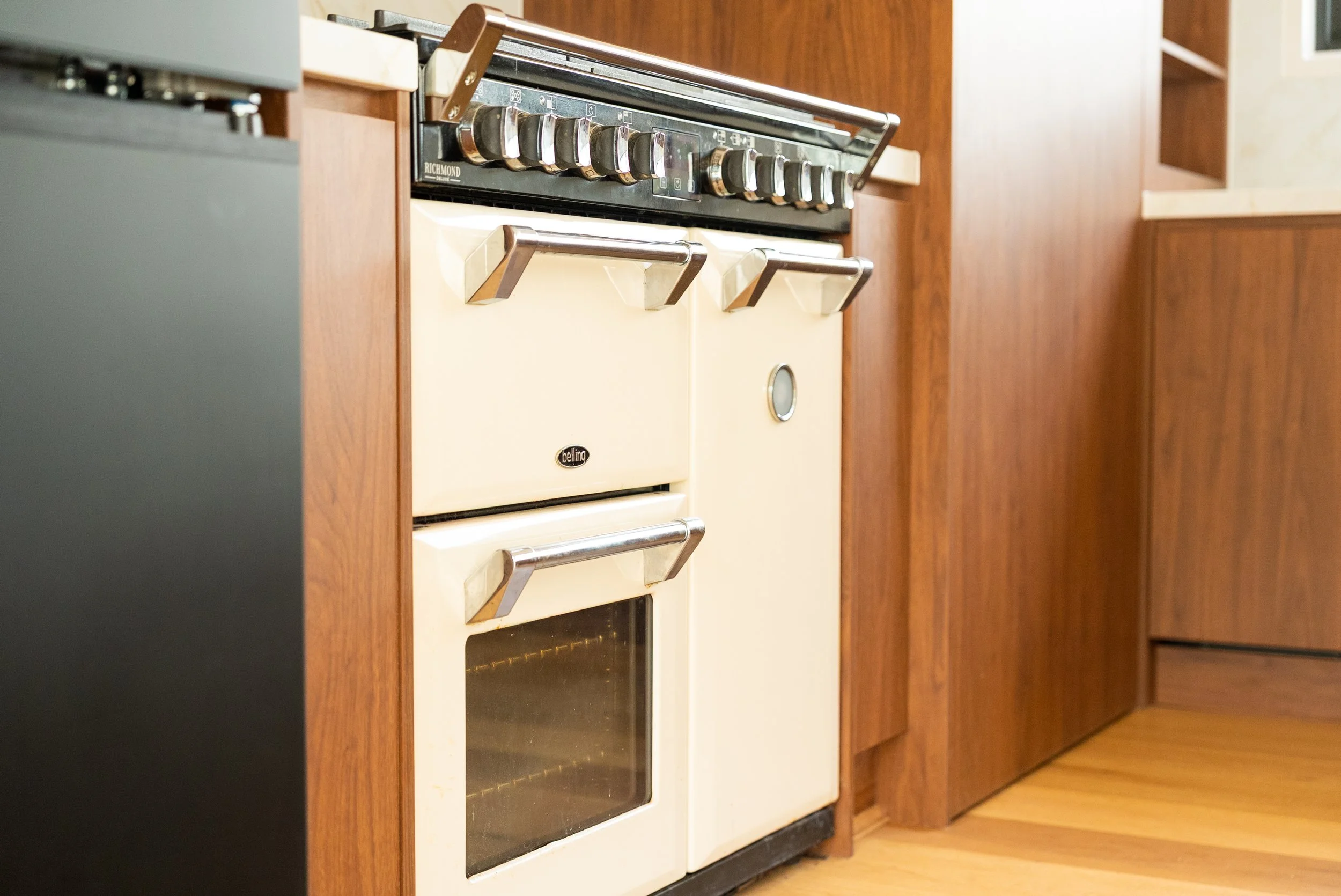 Vintage cream-colored stove with metal handles, situated in a kitchen with wooden cabinetry and a hardwood floor.