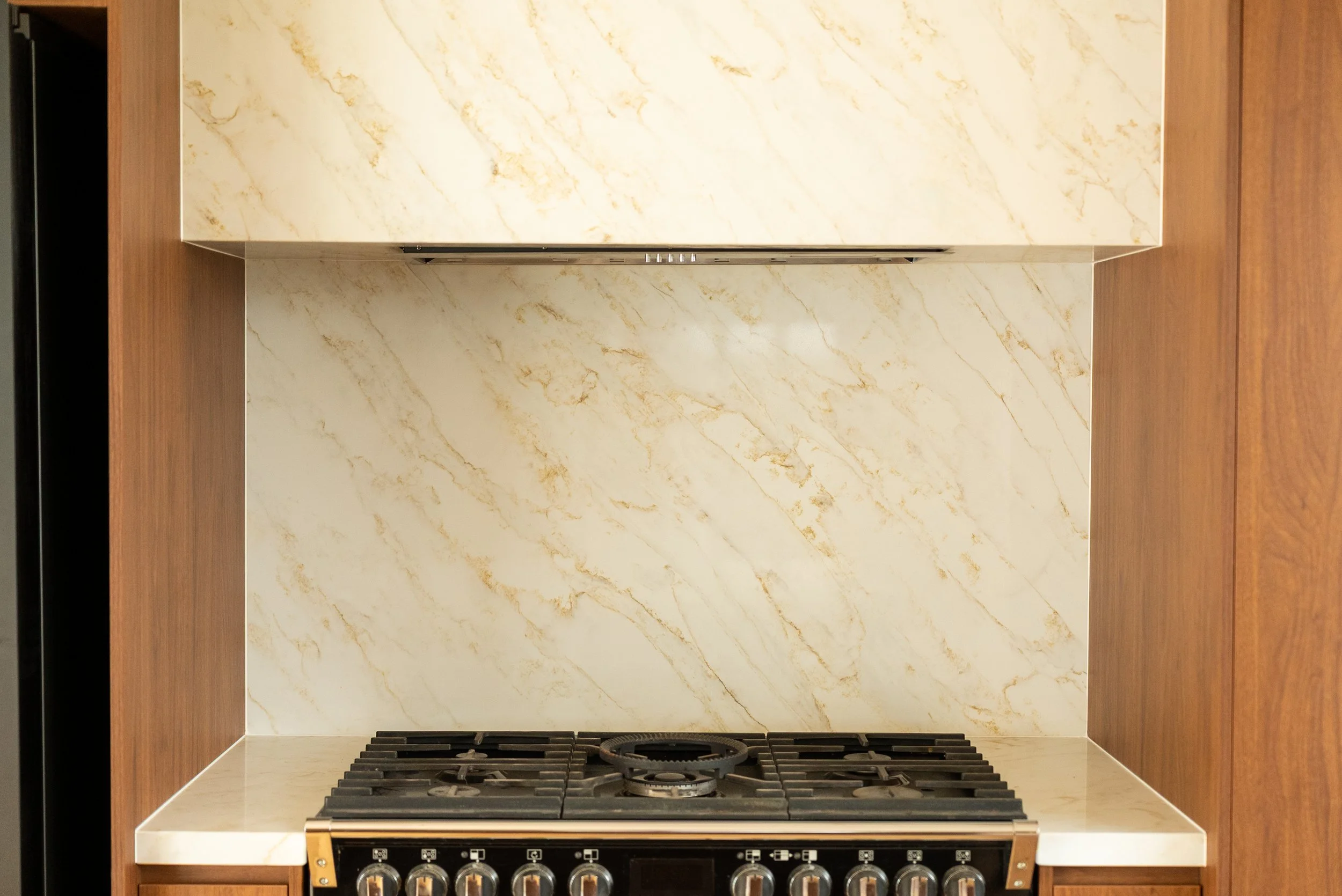 Kitchen stove with four burners, a marble countertop, and a marble backsplash, with wooden cabinets on each side.