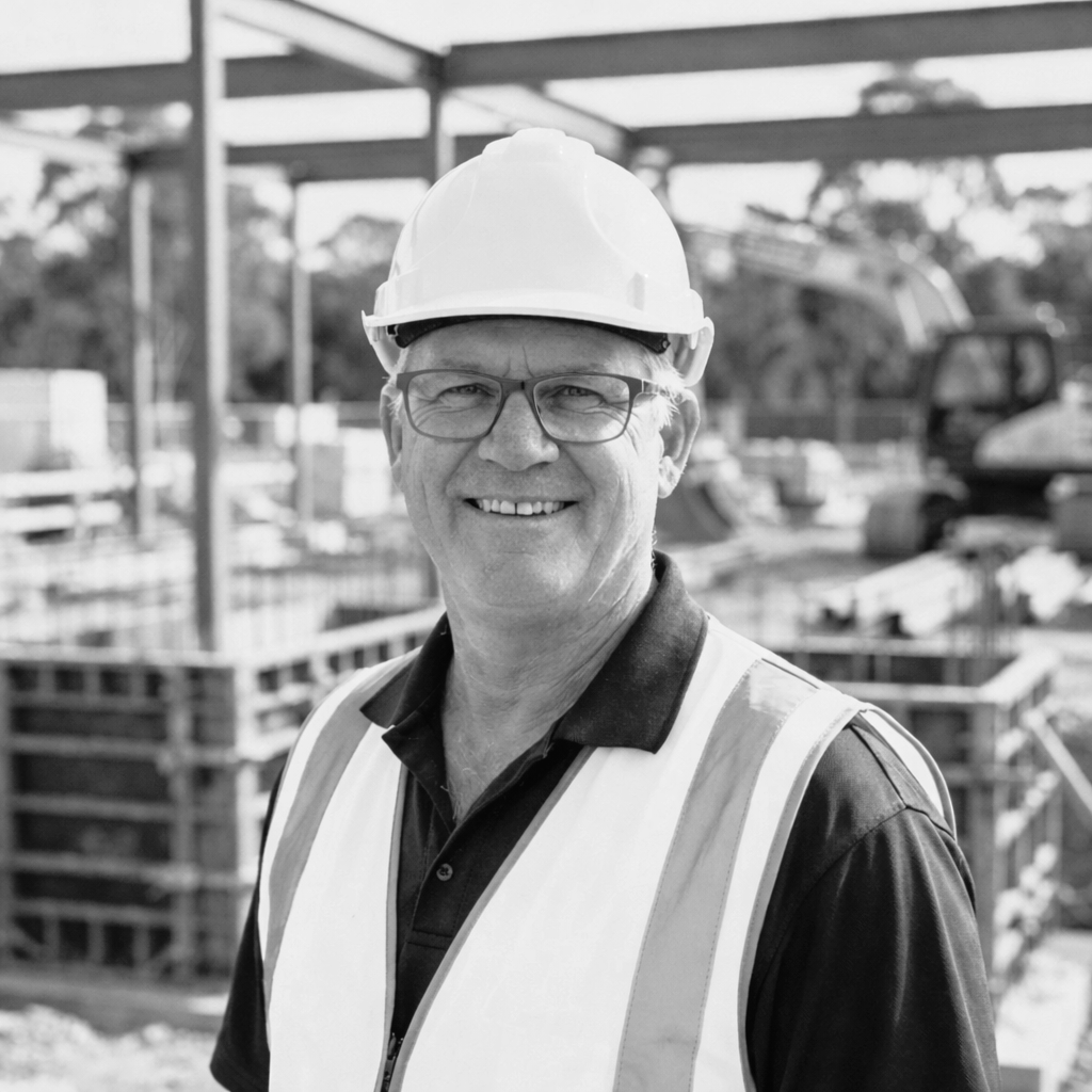 A smiling construction worker wearing a hard hat and safety vest at a construction site.