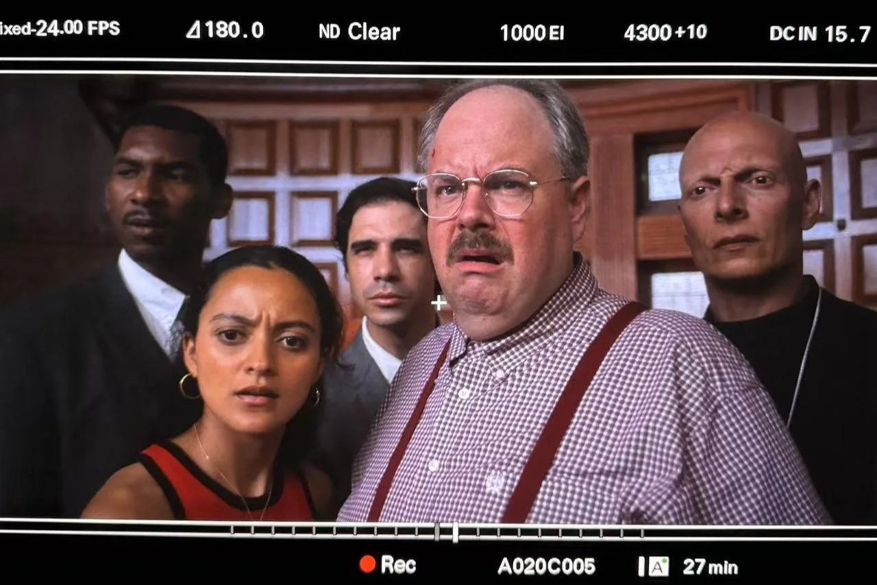 A group of five people looking surprised or confused, inside a wooden-paneled room.