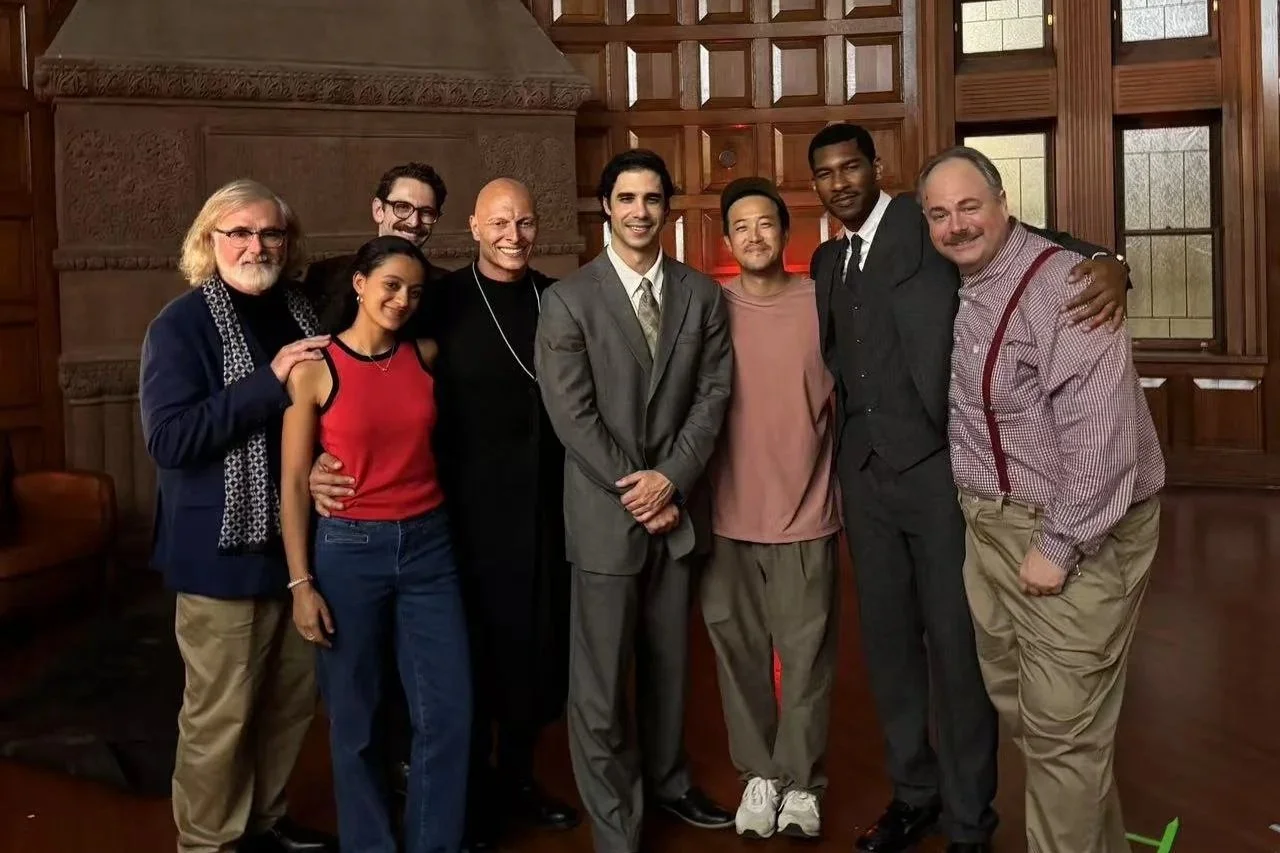 A group of nine diverse people standing together in a wood-paneled room, smiling at the camera.