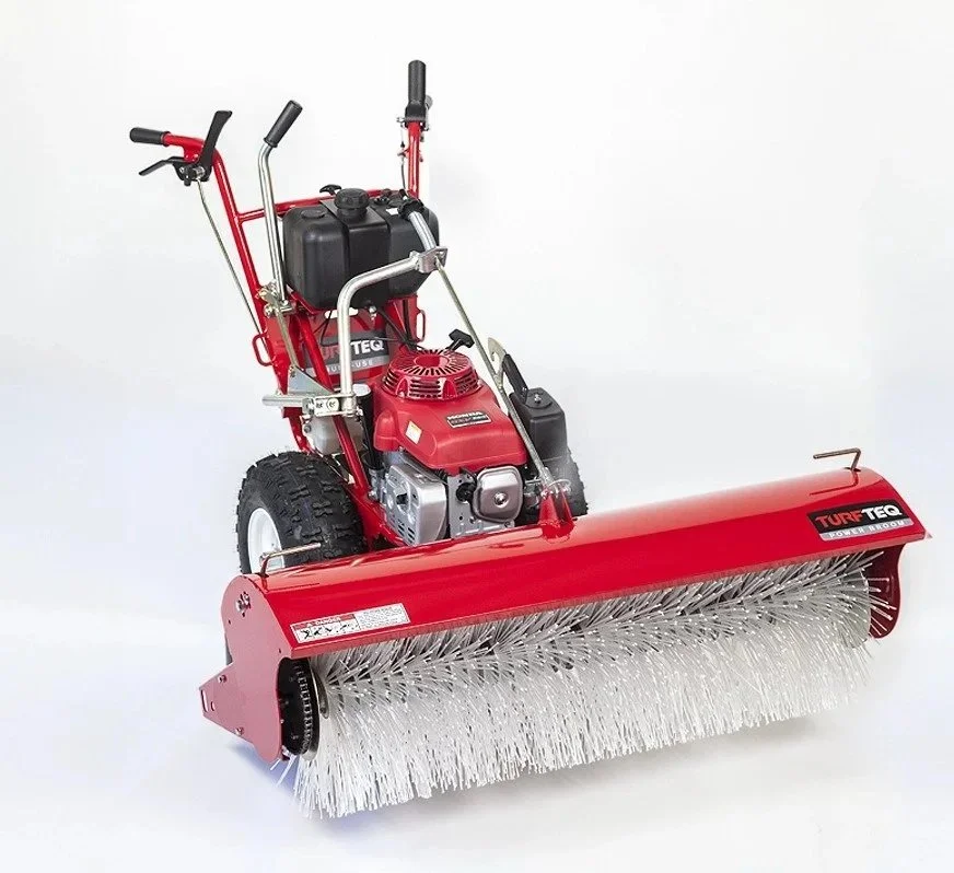 Red walk-behind rotary broom with a gas engine and handlebar, used for sweeping streets or large surfaces, with a cylindrical brush underneath.