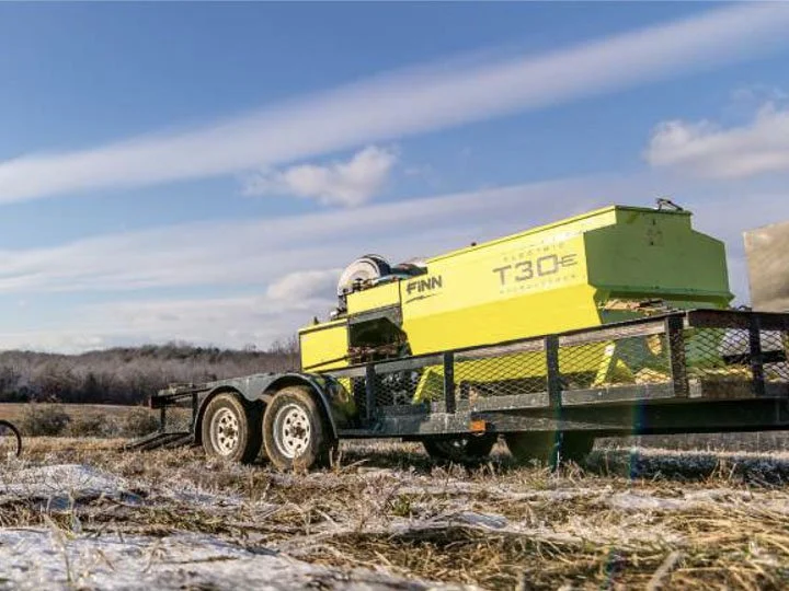 Yellow towable generator on a black trailer parked on a field with snow, under a partly cloudy sky.